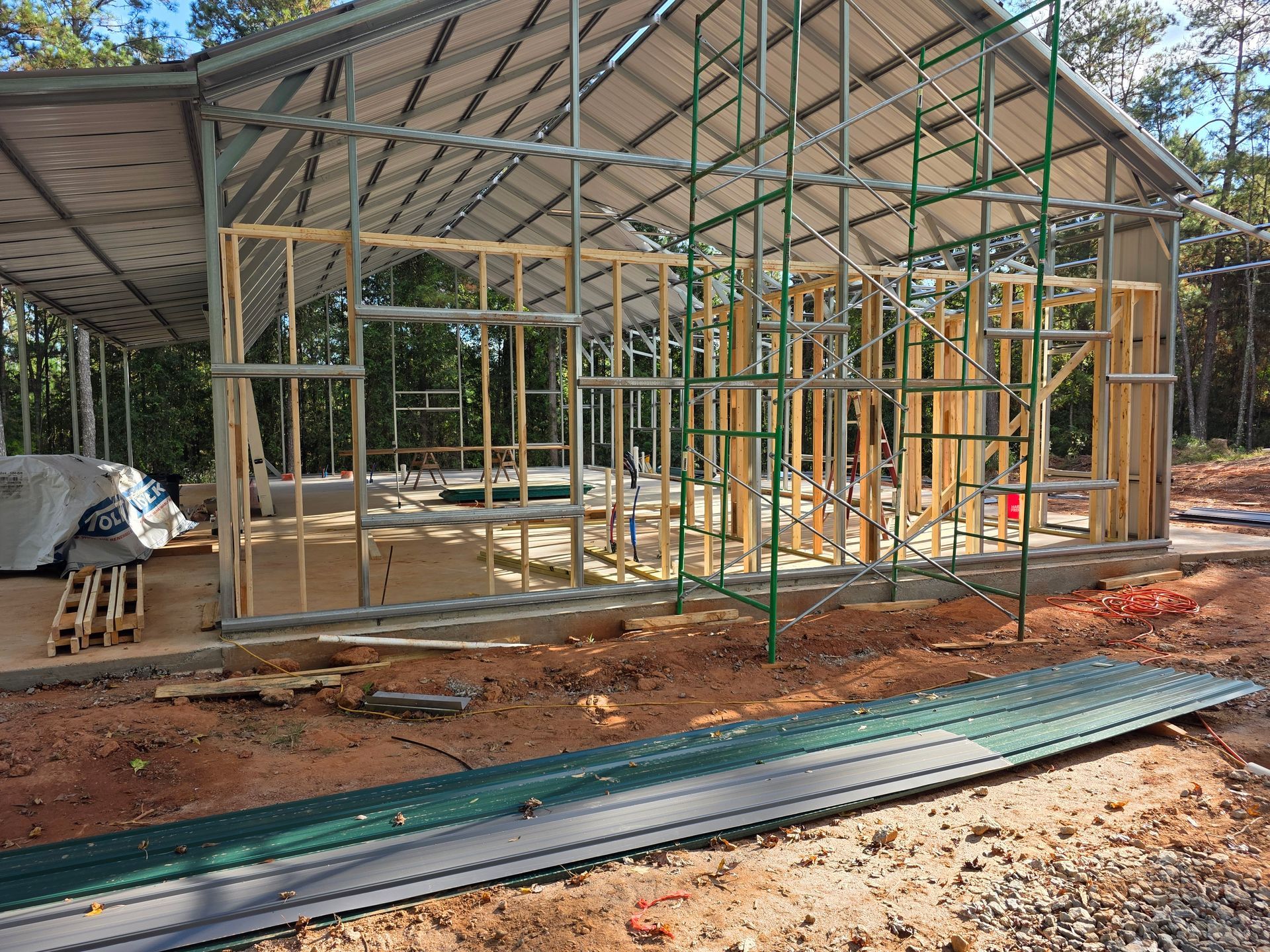 Construction of a metal-framed building with exposed wood framing; green metal roofing; outdoors.
