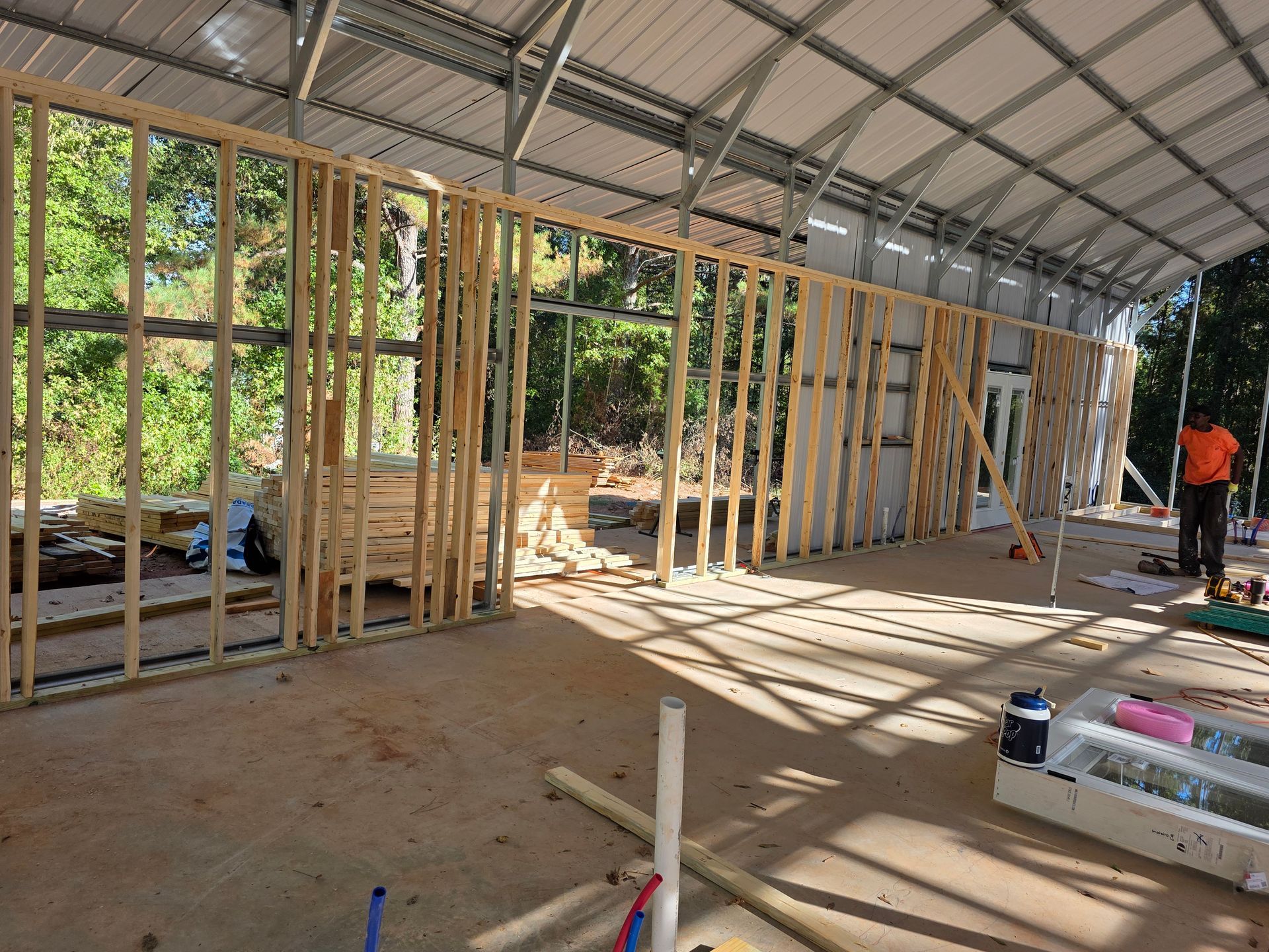Interior view of a building under construction, featuring wooden framing inside a metal structure with natural light.