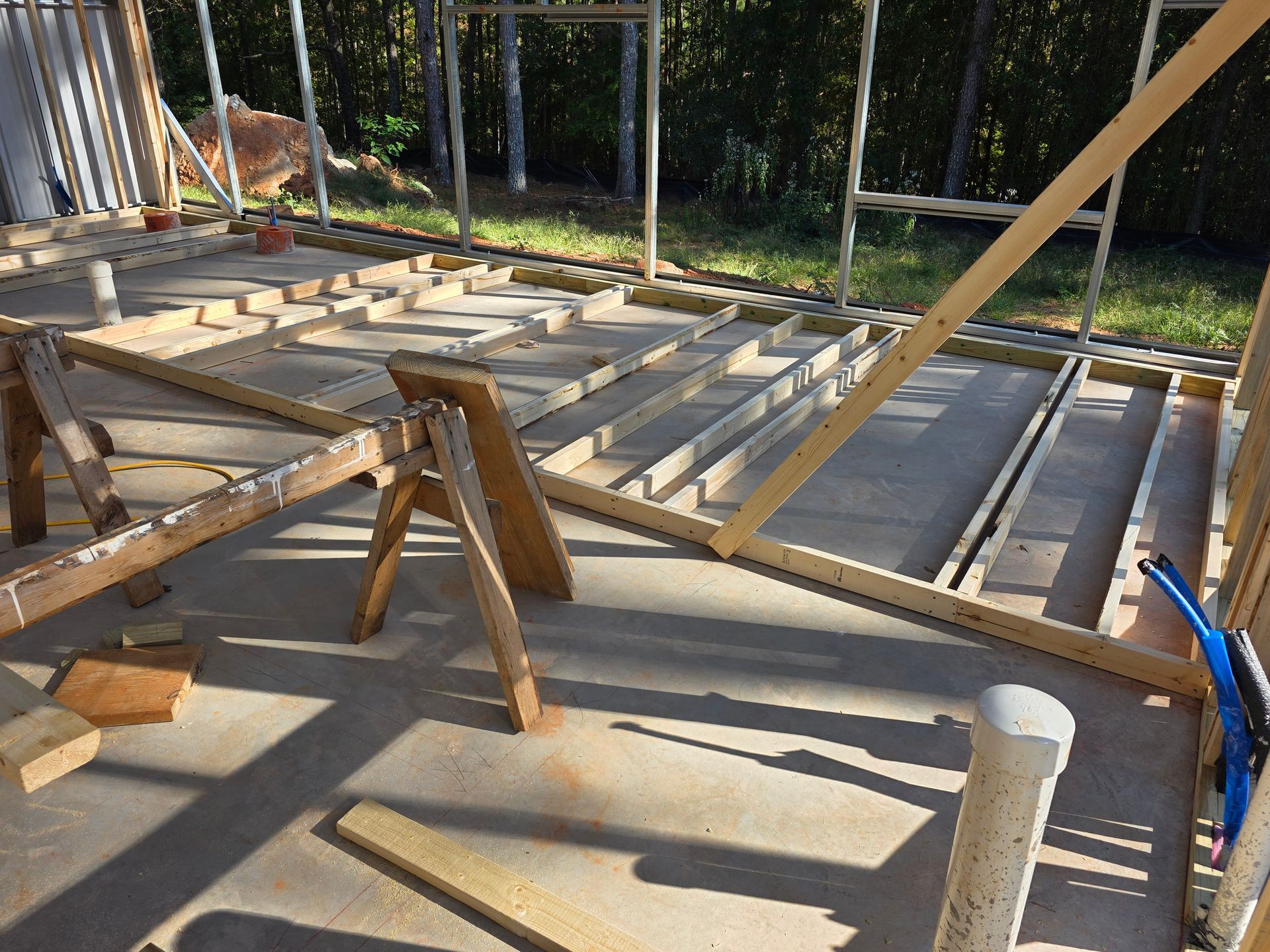 Construction site interior; wooden frame on concrete floor, sawhorse, sunlight.
