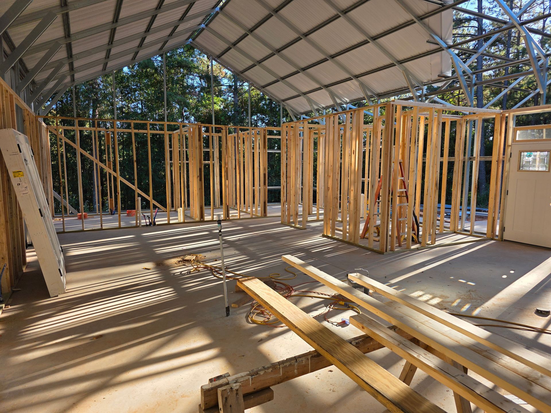 Interior view of a building under construction. Wooden framing is set up with an open metal roof overhead.