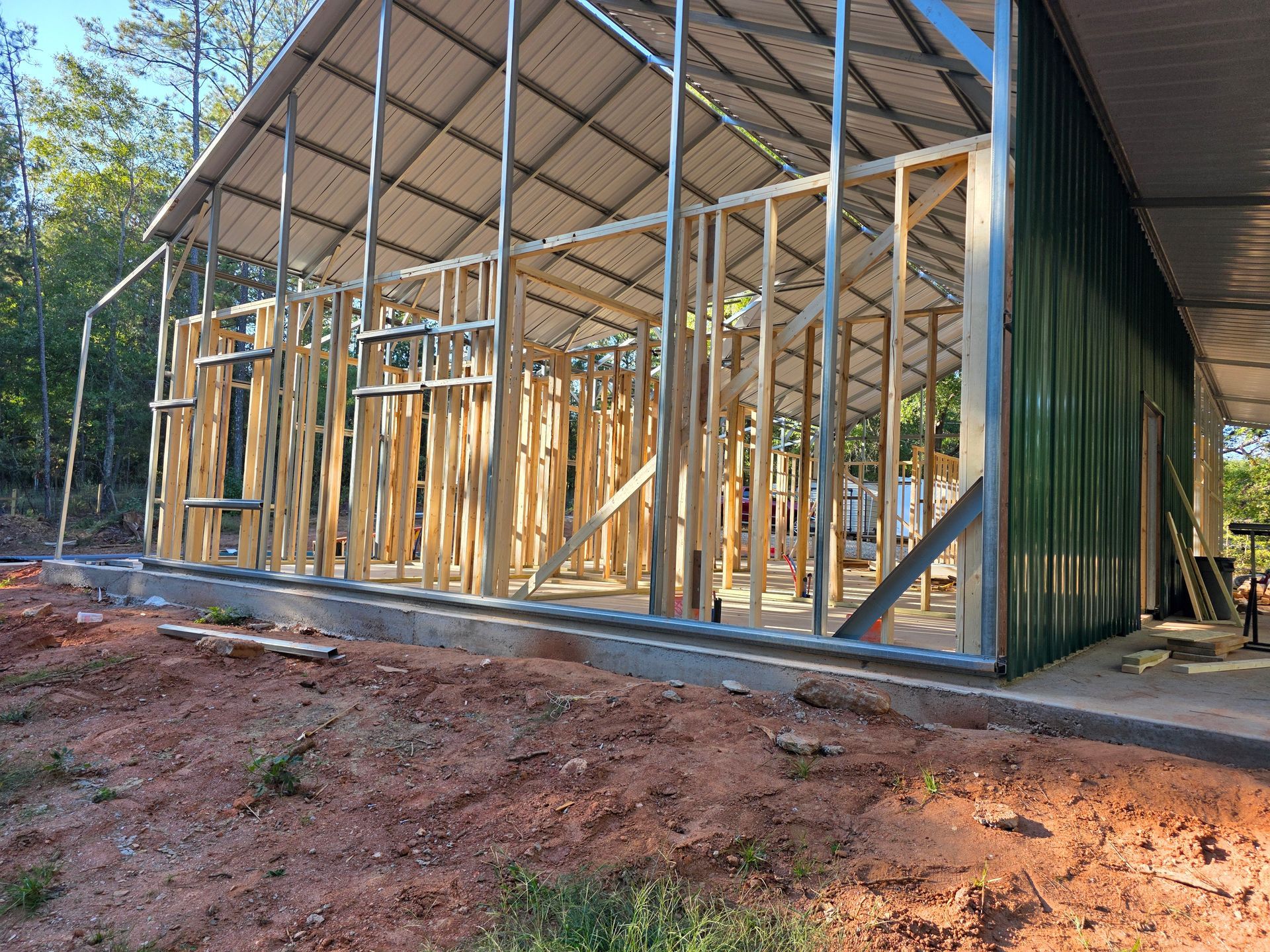 Construction site with a partially framed wooden structure. Green metal siding and a metal roof are visible.