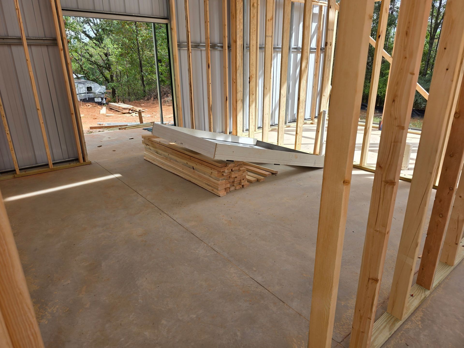 Interior of a building under construction, showing wooden studs, concrete floor, and stacked lumber.
