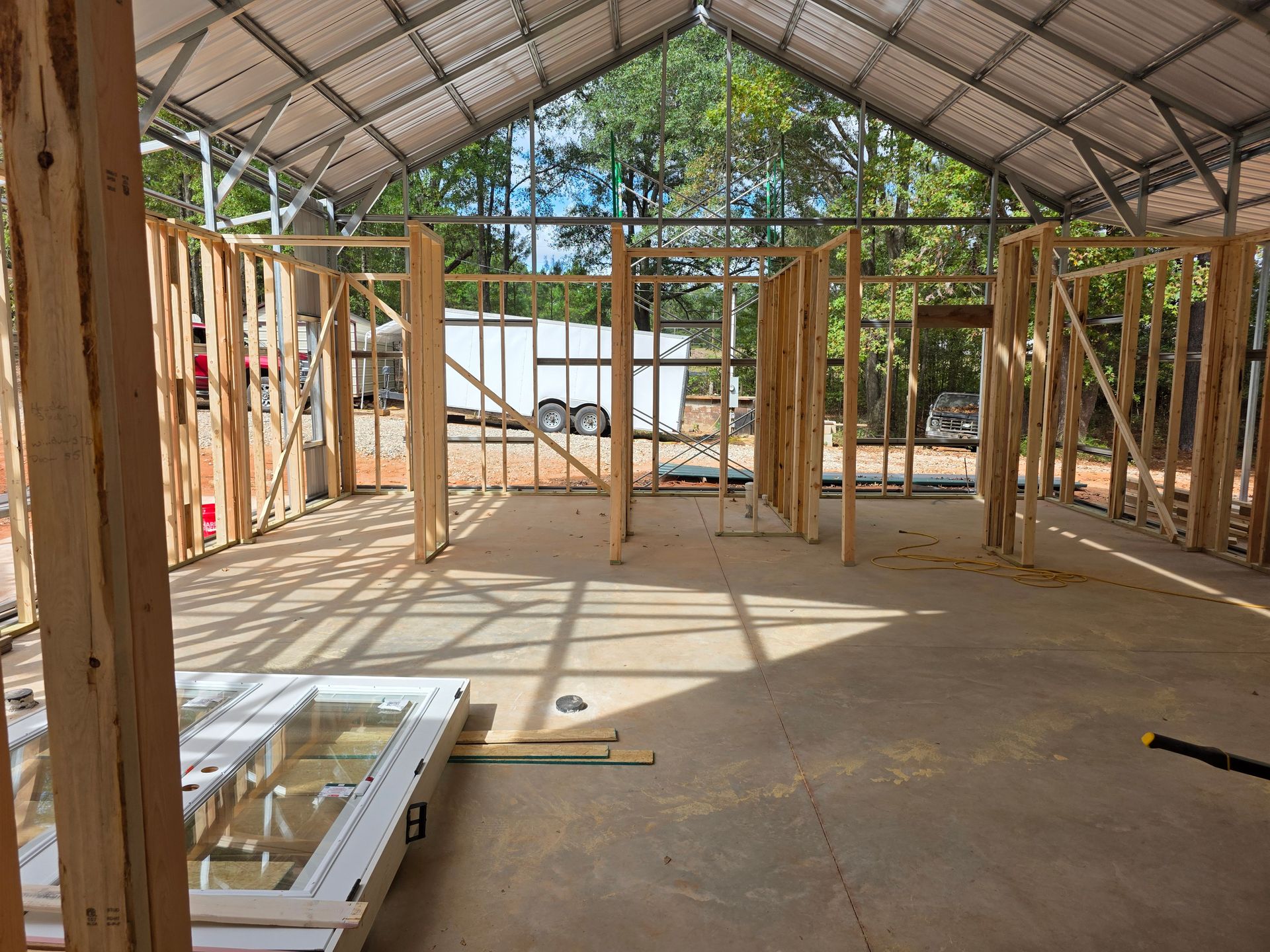 Interior view of a building under construction, showing wooden frames and an open roof, with a trailer visible outside.