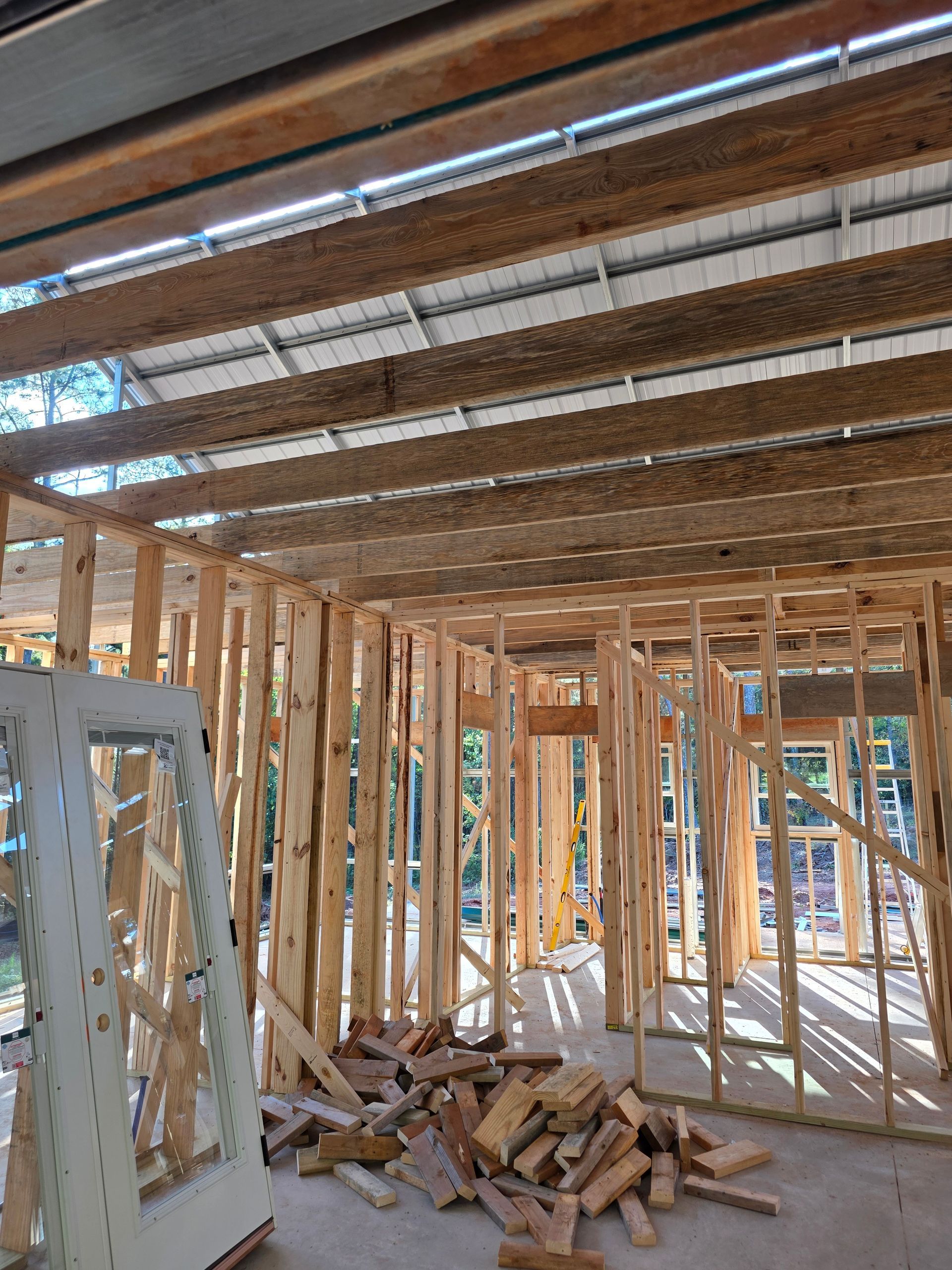 Interior view of a building under construction, showing wooden framing, roof beams, and a doorway.