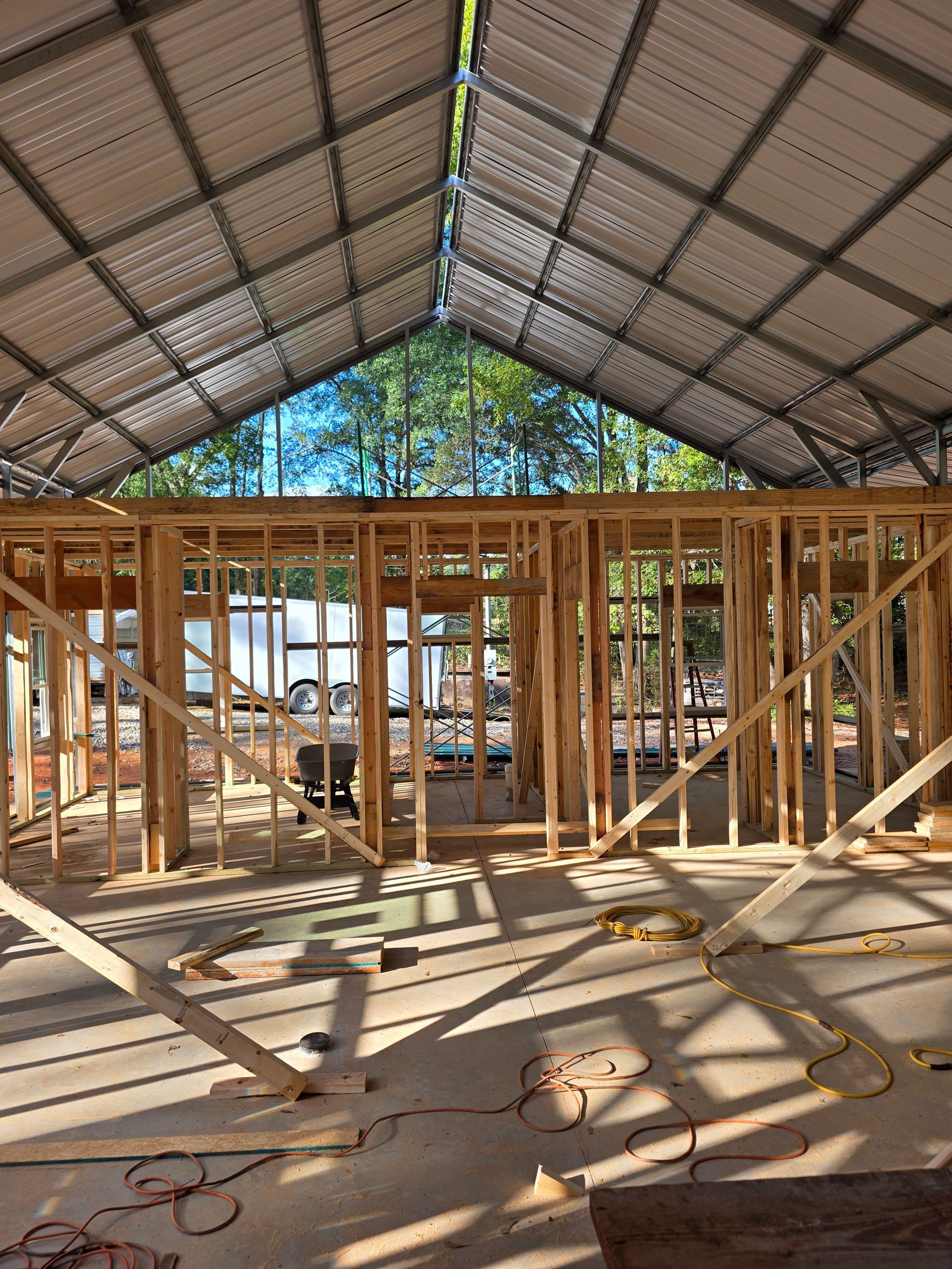 Wooden framing inside a metal-roofed building under construction. Sunny daylight.
