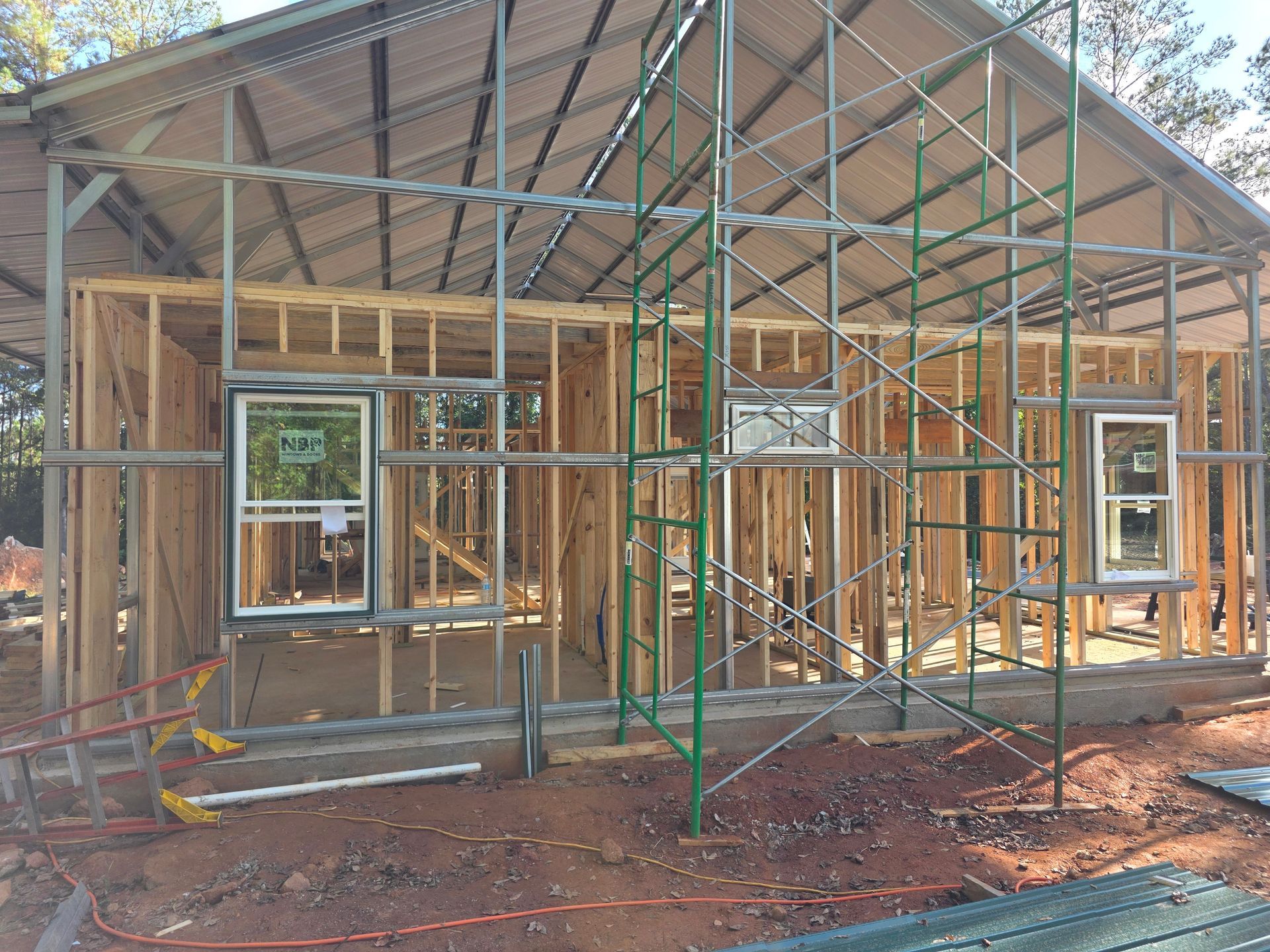 House under construction, wood framing with a metal roof and scaffolding.