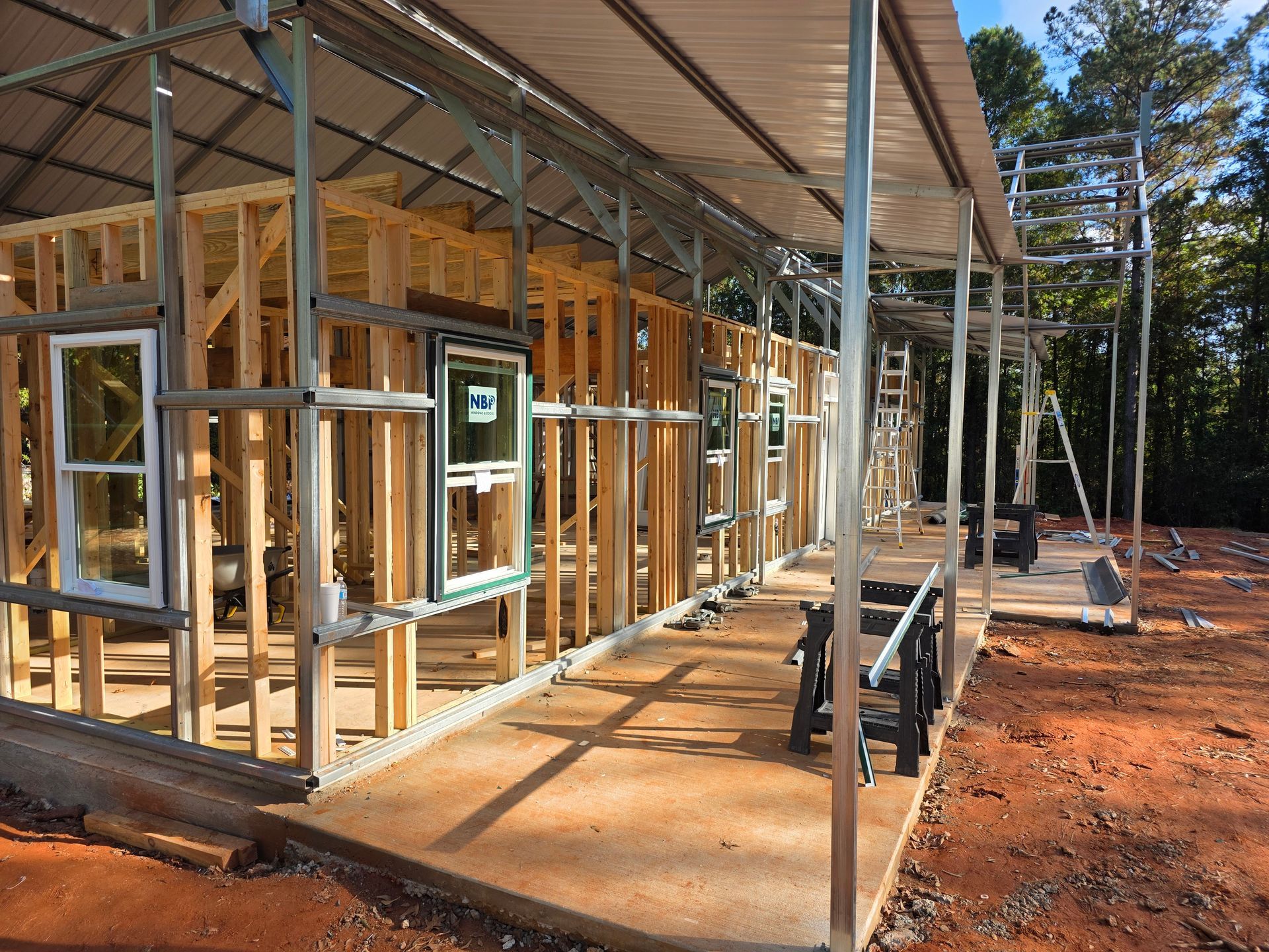 Construction of a wood-framed building with windows, under scaffolding. The ground is reddish dirt.