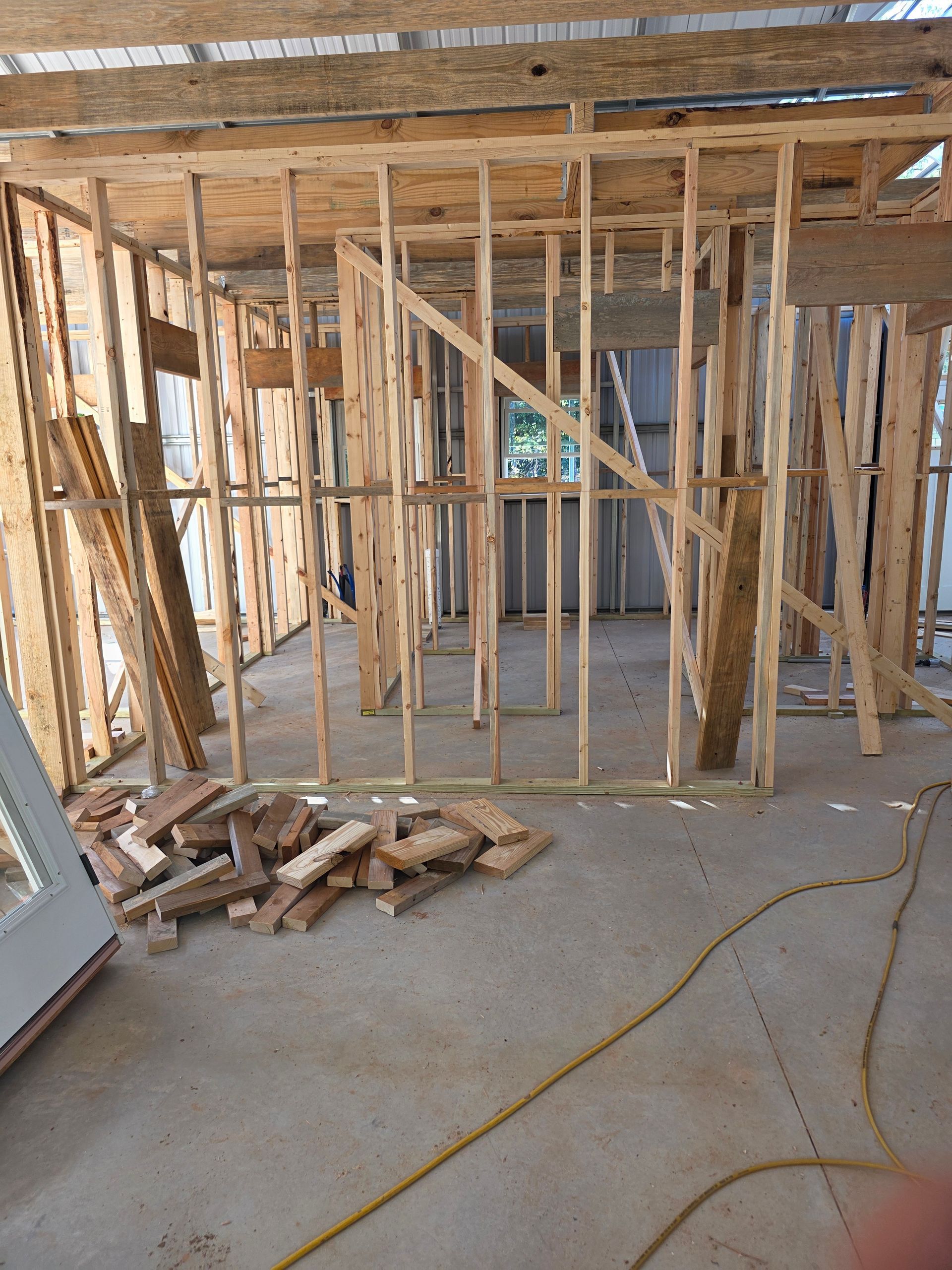 Interior of a room under construction, with wooden frame walls, concrete floor, and scattered wood pieces.
