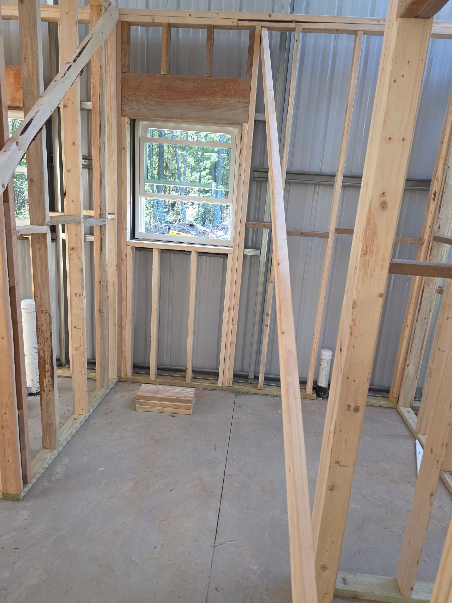 Interior of a room under construction, with wooden frame, window, and metal siding.