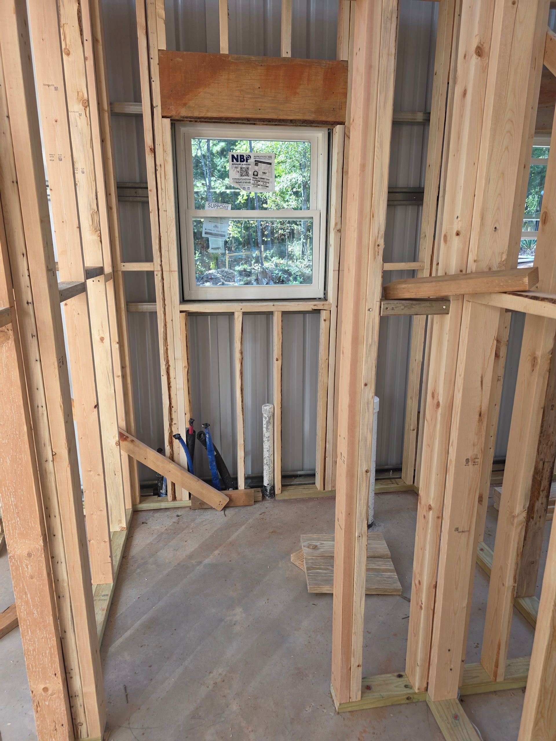 Interior of a building under construction. Wood framing surrounds a window with a view to the outside.