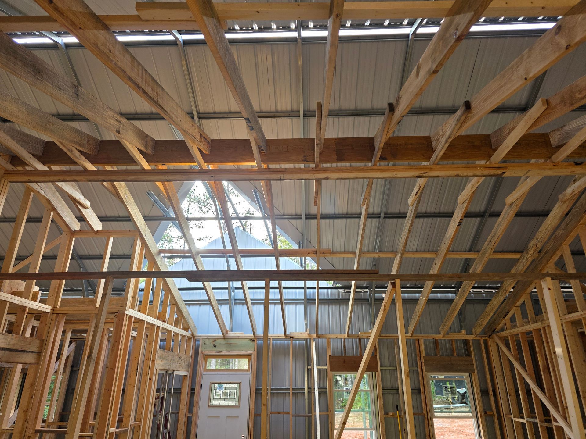 Interior view of a building under construction, showing wooden framing and exposed metal roof.