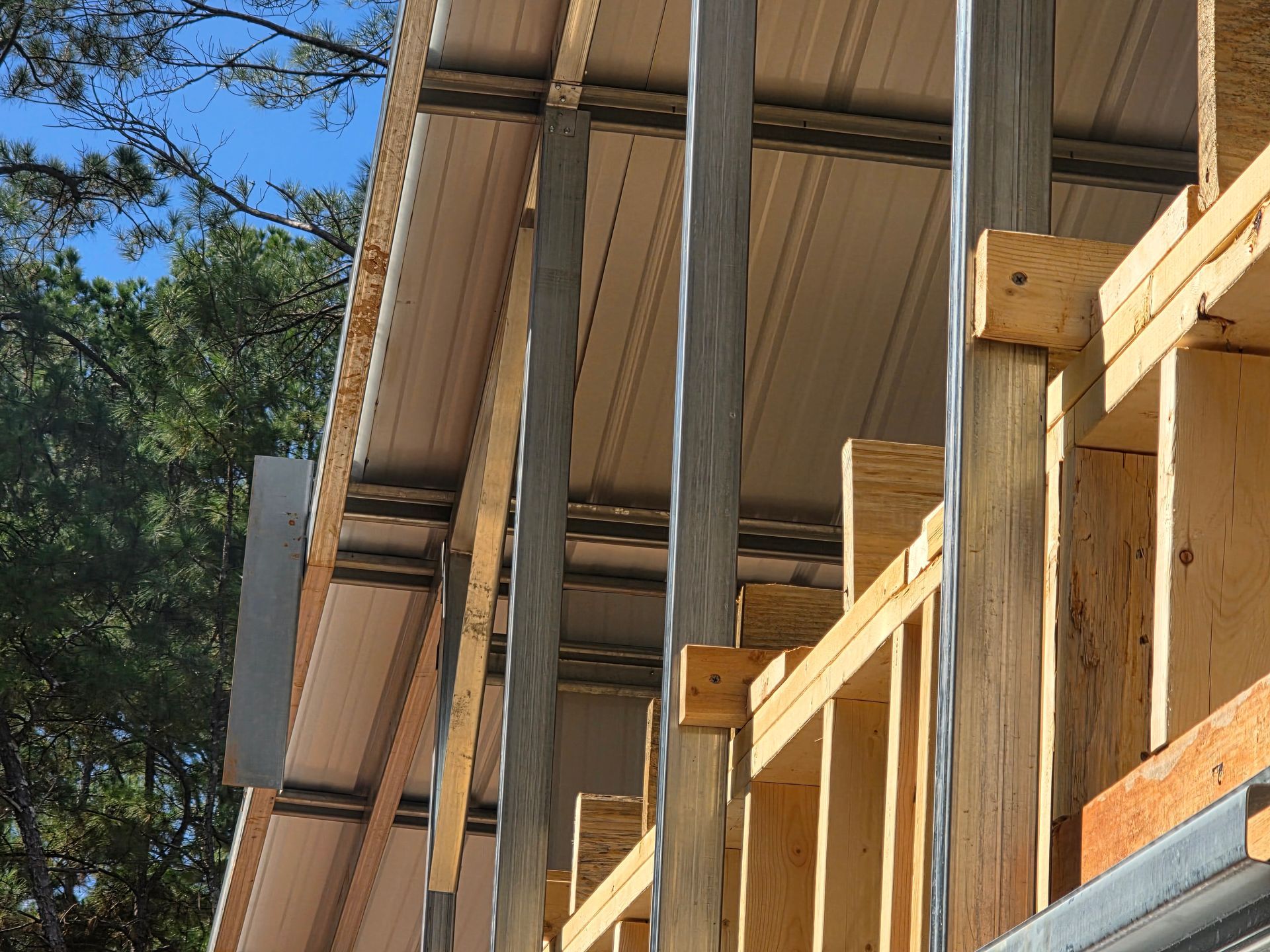 Wood-framed building under construction with metal supports and roofing, blue sky background.