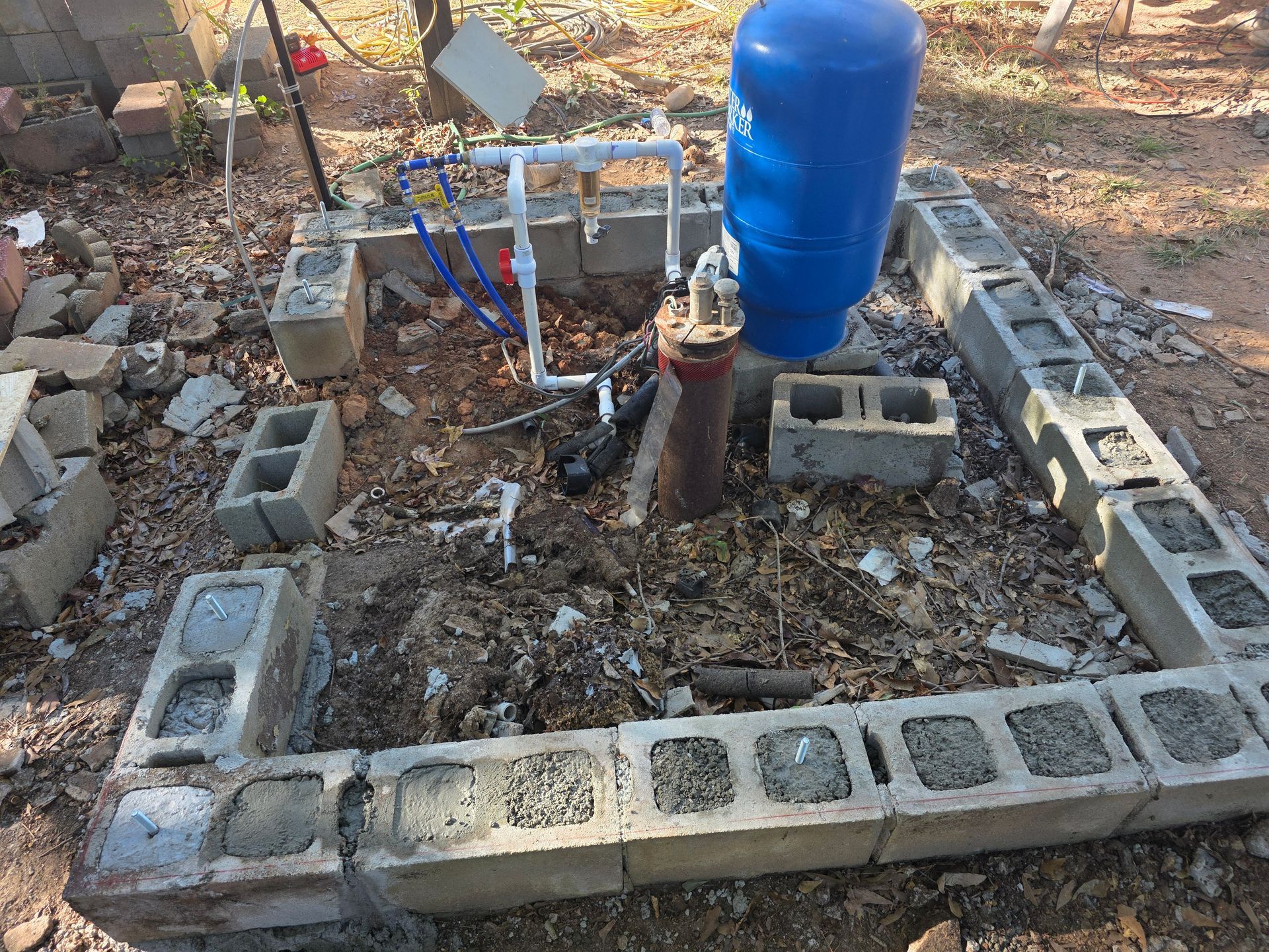 A well pump system in a concrete block enclosure, featuring a blue pressure tank and piping.
