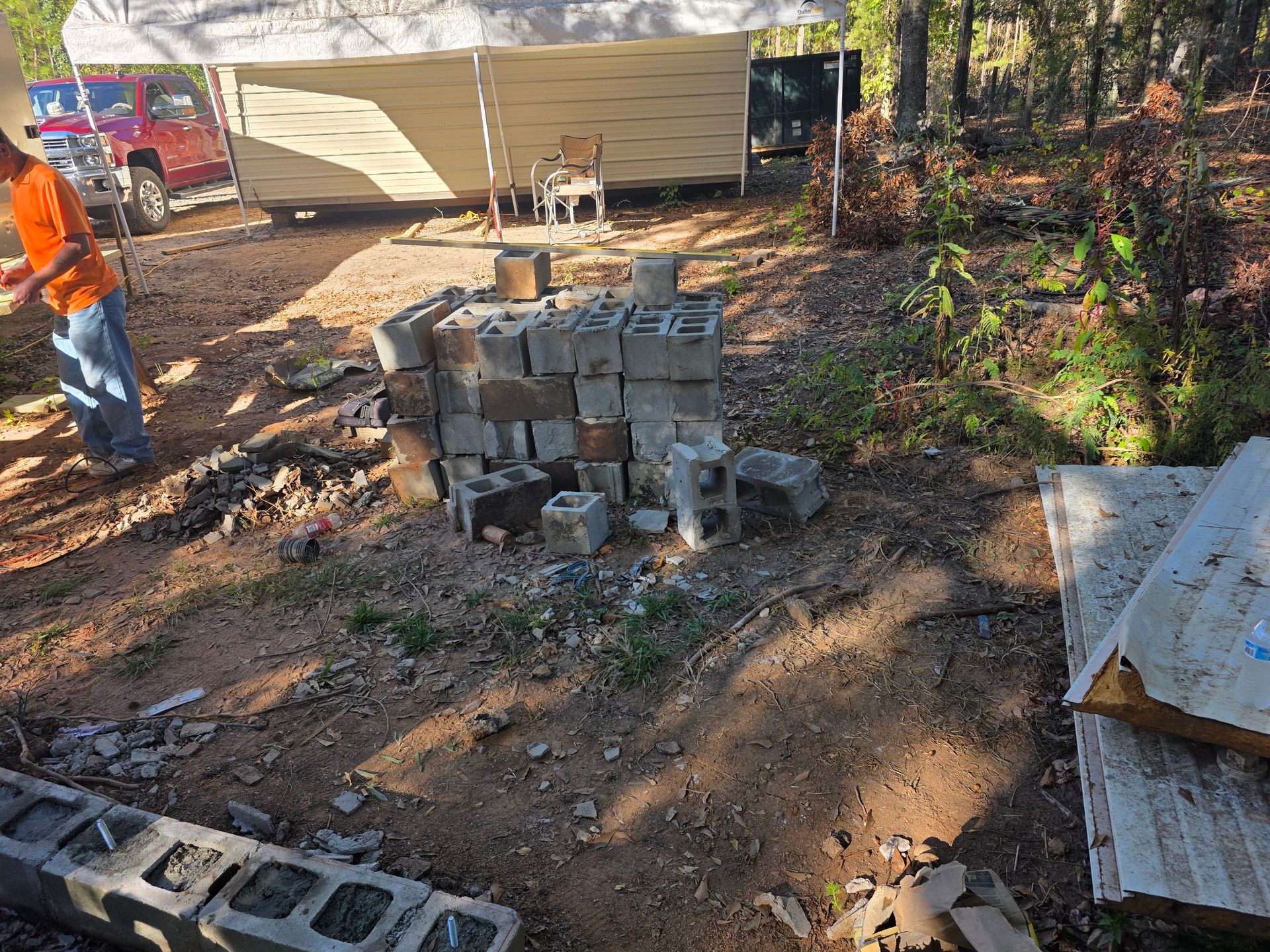 A pile of cinder blocks with a person nearby and a white canopy in an outdoor setting.