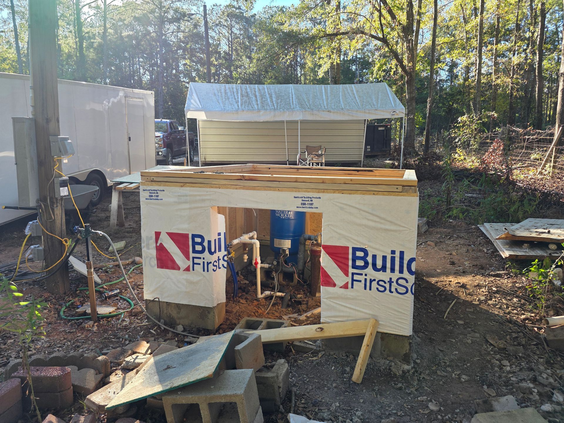 Construction site with a partially built structure, possibly a well house, wrapped in building paper.