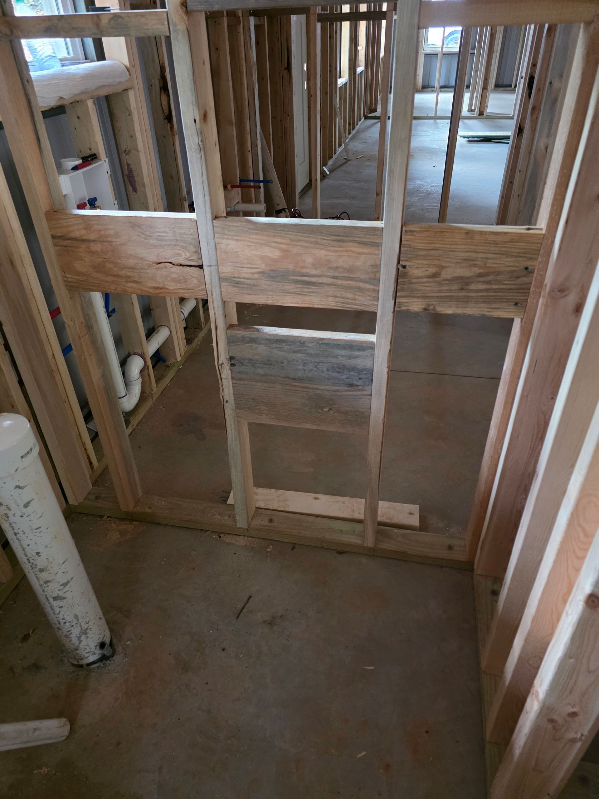 Interior view of wooden framing in a construction site with open doorway and concrete floor.