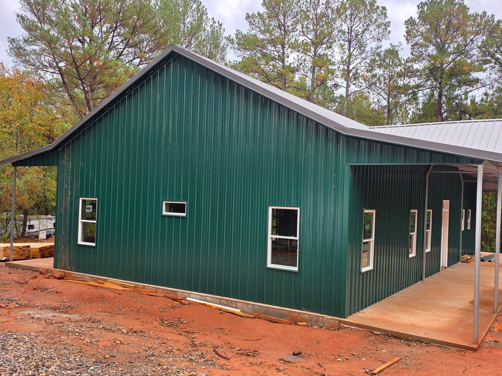 Green metal building with white-trimmed windows and a covered porch, set on a red dirt ground.