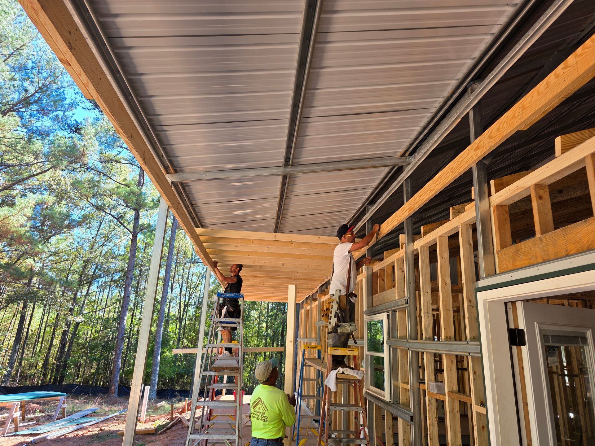 Construction workers installing metal roofing on a wood-framed structure in an outdoor setting.