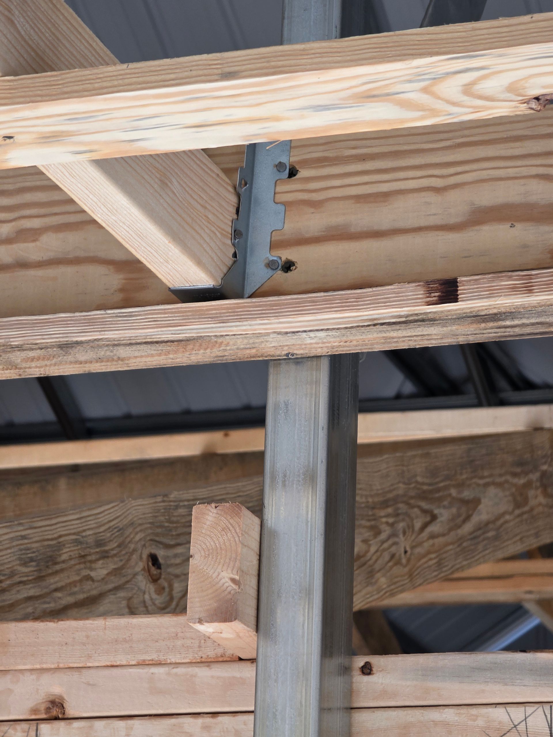 Close-up of wooden rafters and a metal joist hanger connecting a beam and rafter.