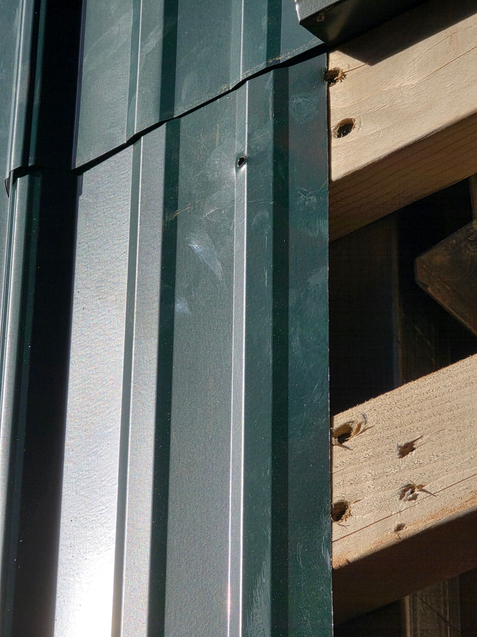Green metal siding next to exposed wooden beams, with visible screw heads.