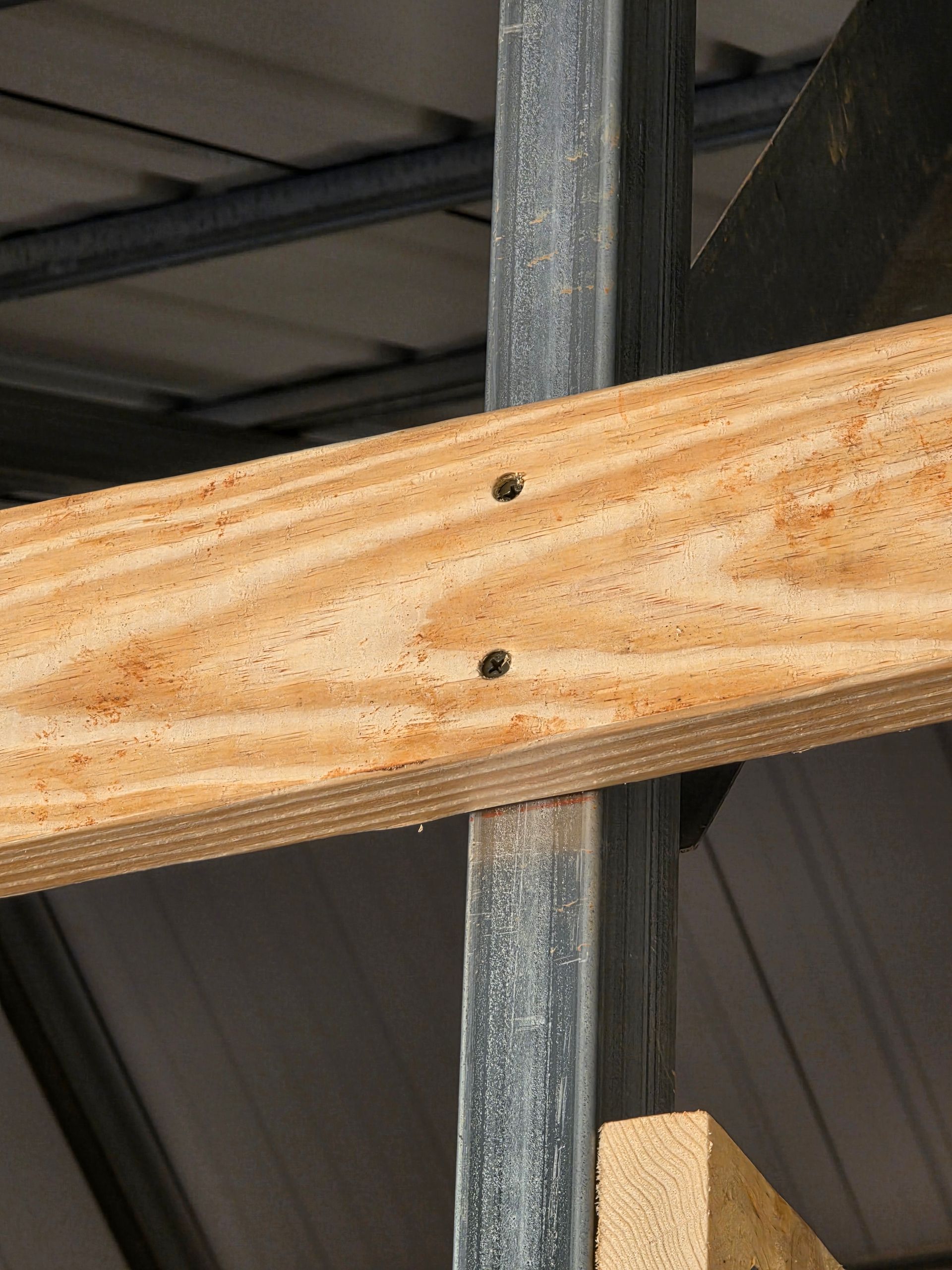 Wood beam attached to a metal post with two screws, set against a metal structure.