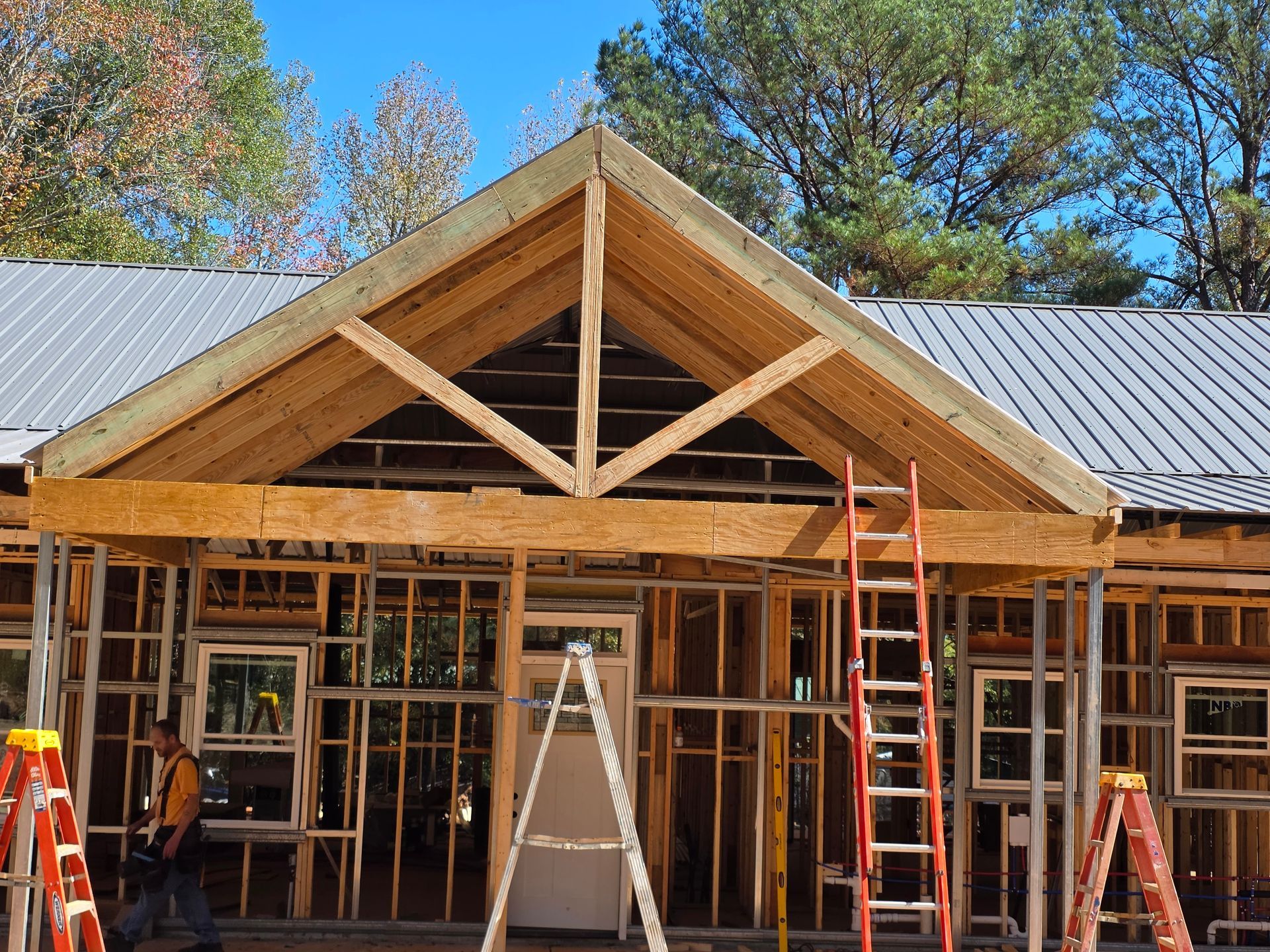Construction of a wooden building with a peaked roof. A ladder and workers are visible.