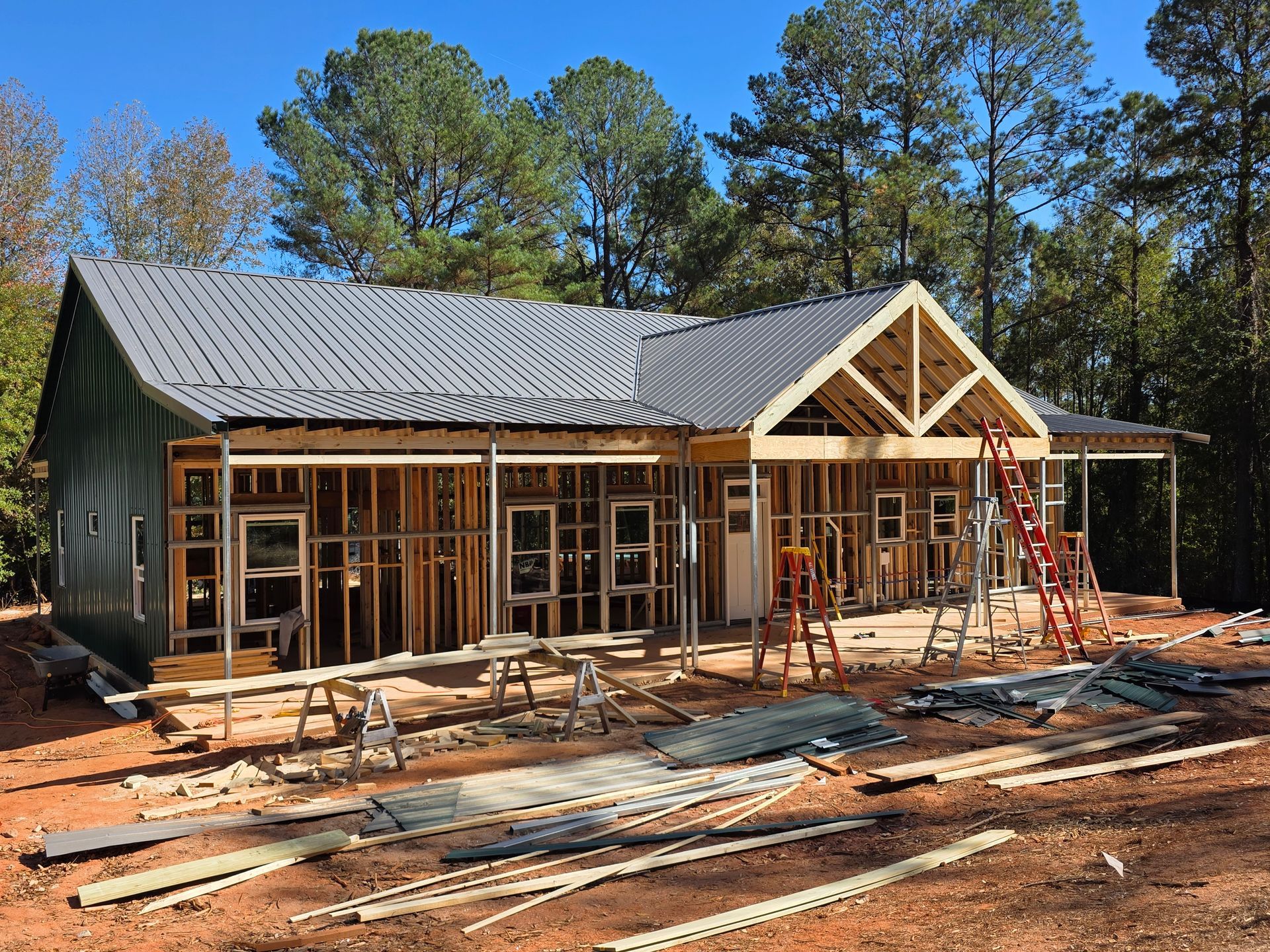 Construction of a house: wooden frame, metal roof, surrounded by tools and materials.