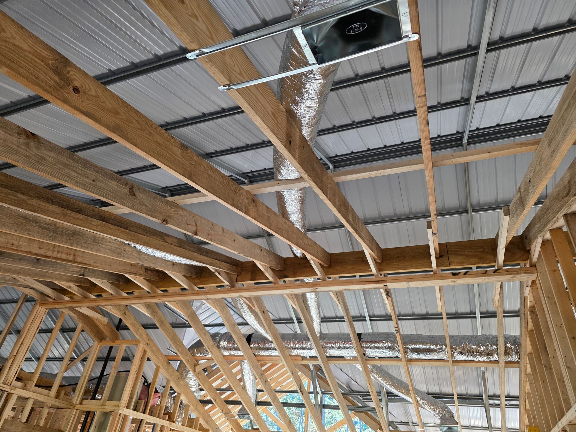 Interior construction of a building with exposed wooden beams, metal roof, and ventilation system.