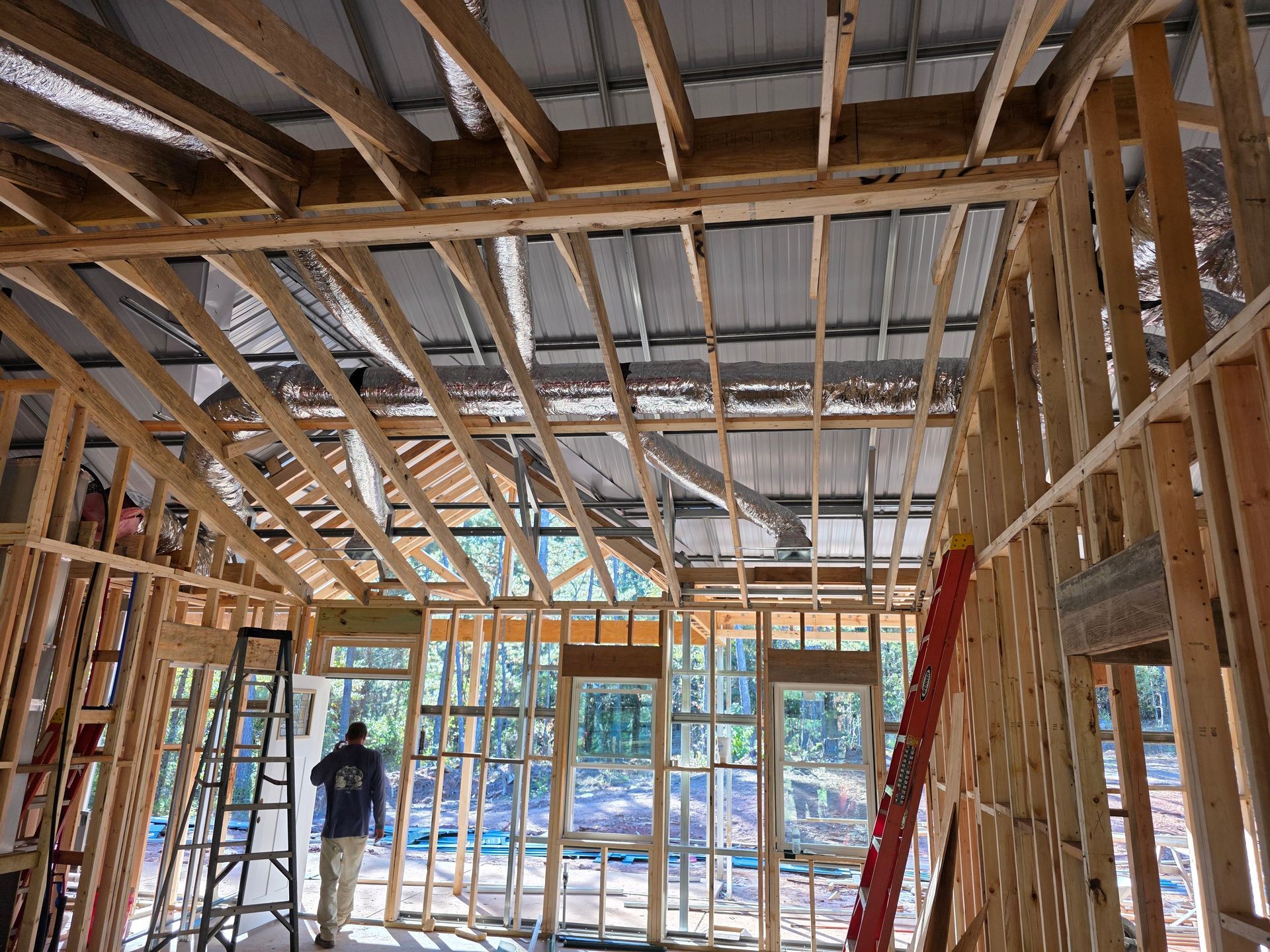 Interior framing of a building under construction, windows, metal roof, person standing, ladder.