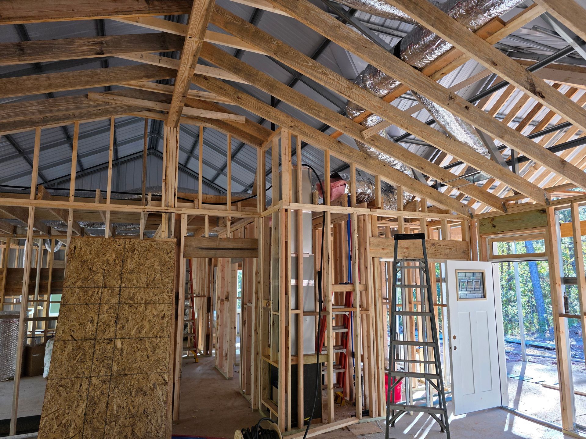 Interior view of a building under construction, showing wooden framing, roof, ladder, and a door to the outdoors.