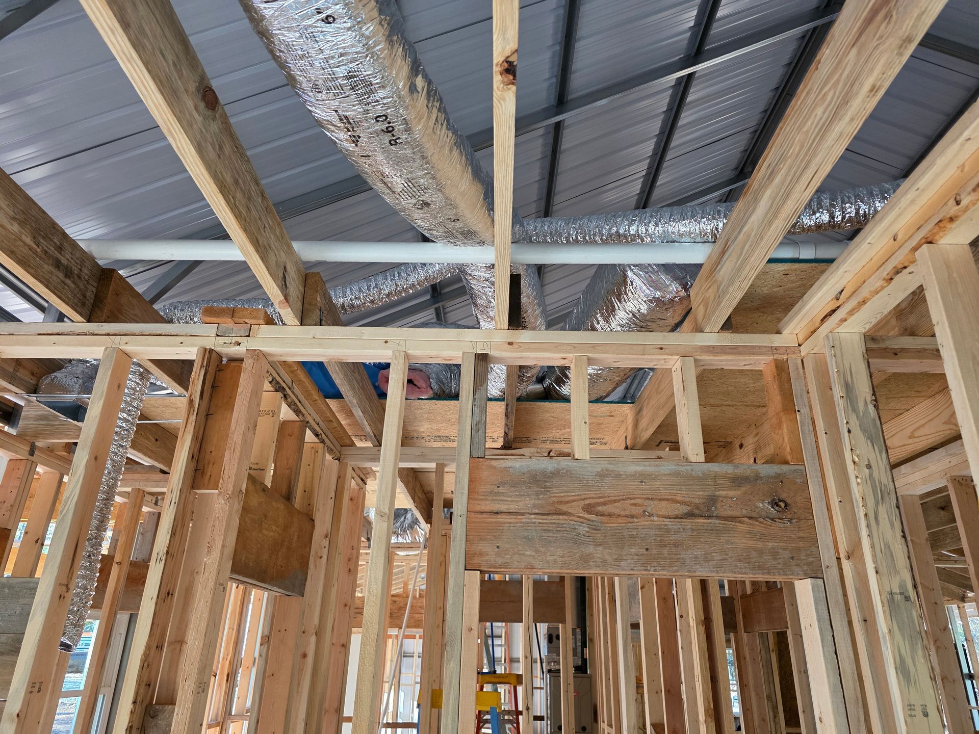 Wooden frame of a building under construction. Ceiling beams, ductwork, and roof visible.
