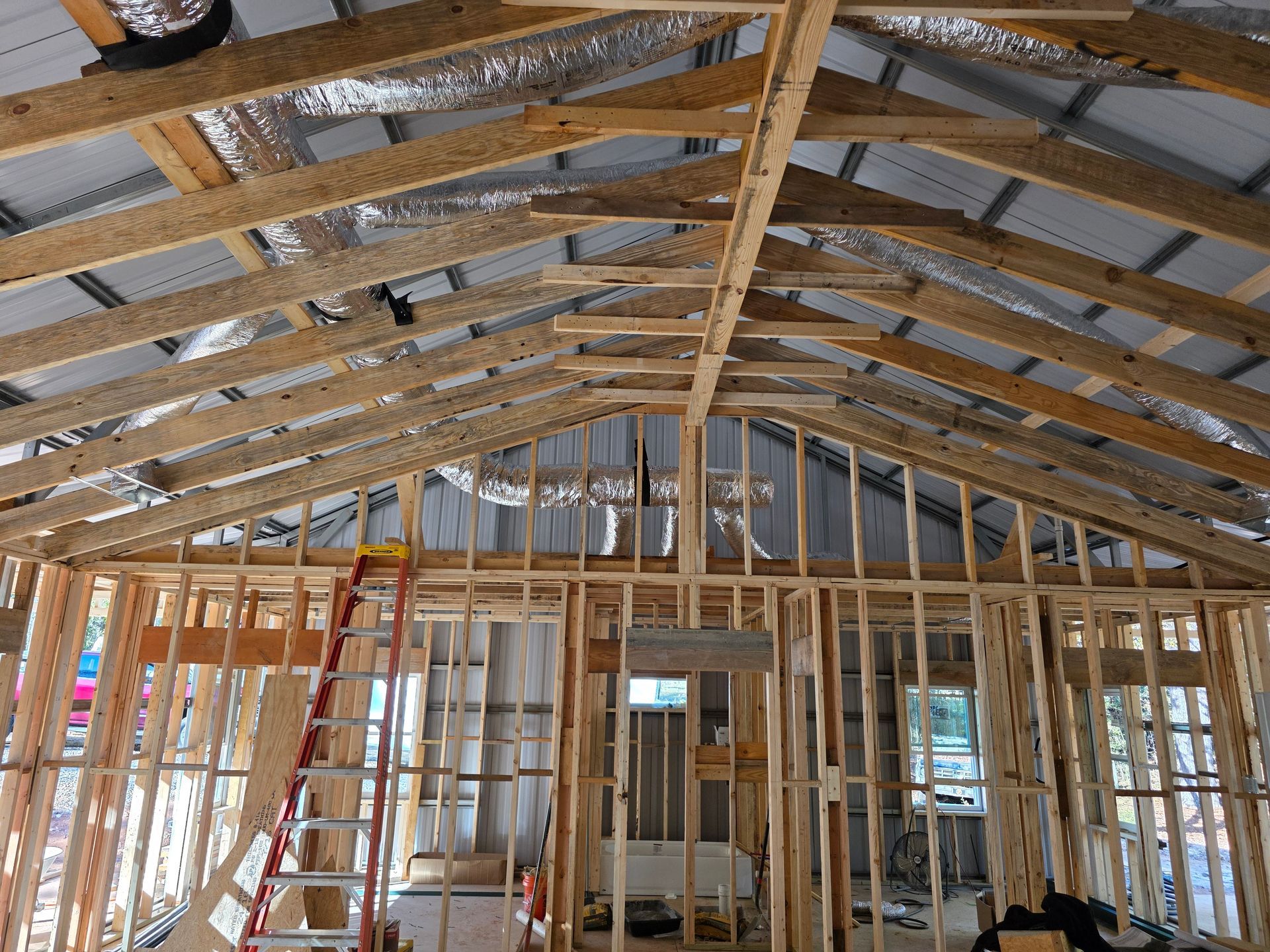 Interior view of a building under construction, showing wooden framing, roof beams, and a ladder.