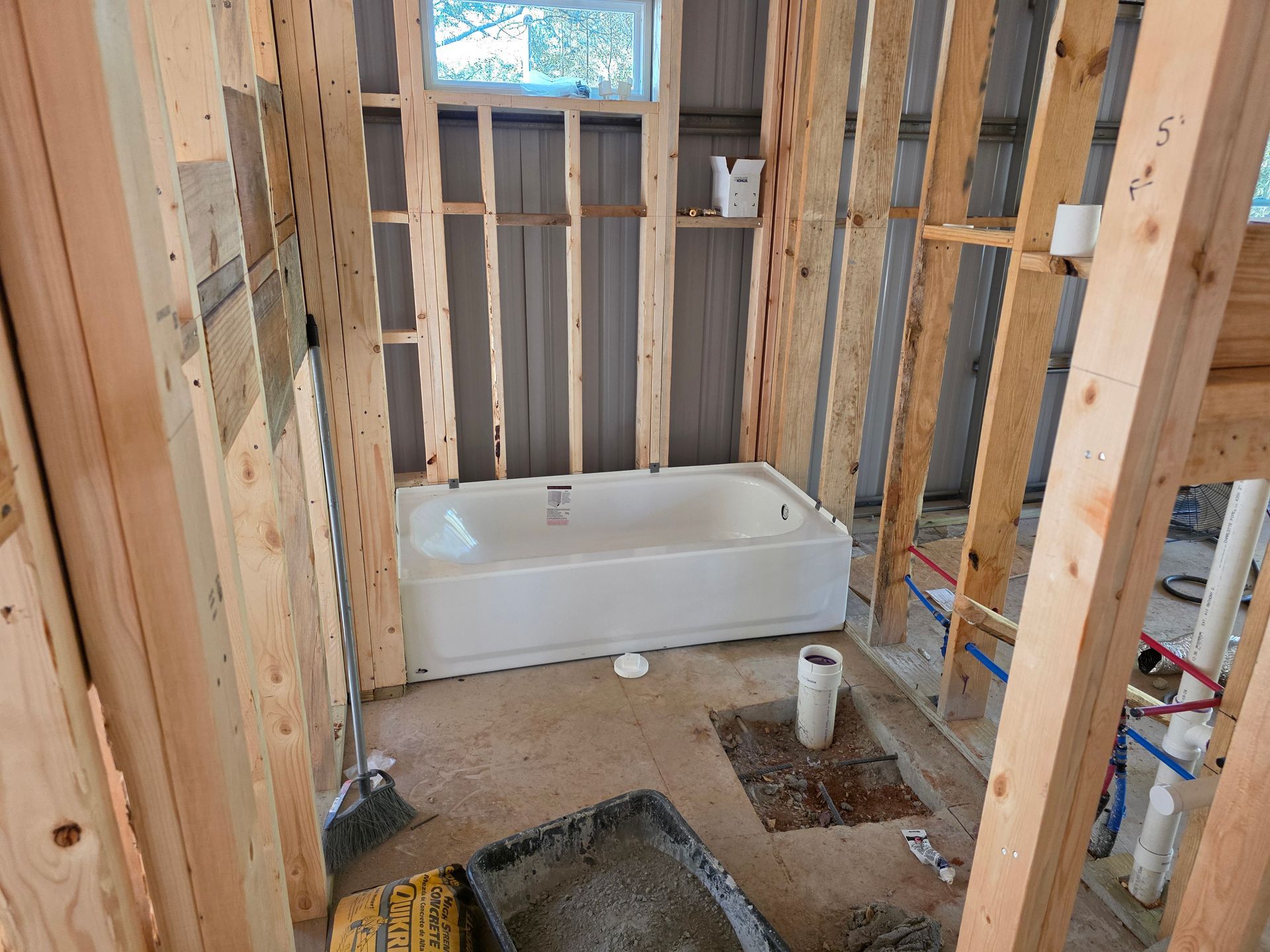 Bathroom under construction with a white bathtub and wooden framing.