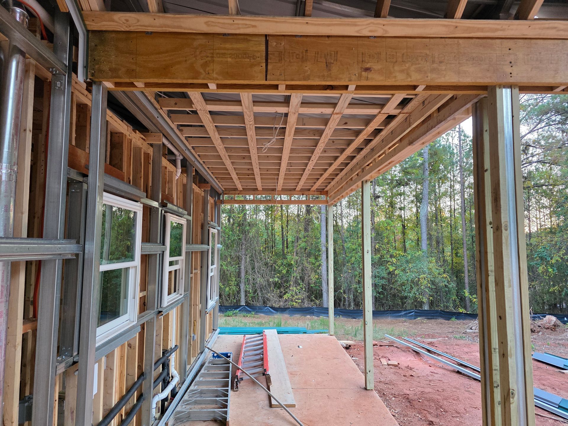 Construction of a porch roof. Wooden framing with exposed joists, metal posts, and side of the house.