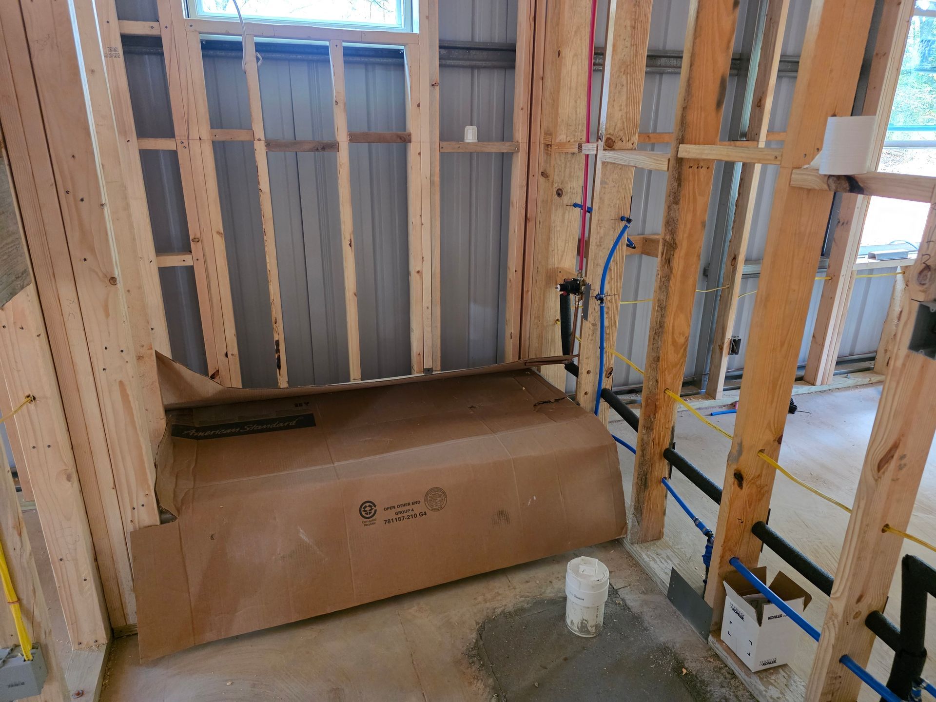 Interior framing of a bathroom with a tub enclosure, plumbing, and electrical outlets visible during construction.