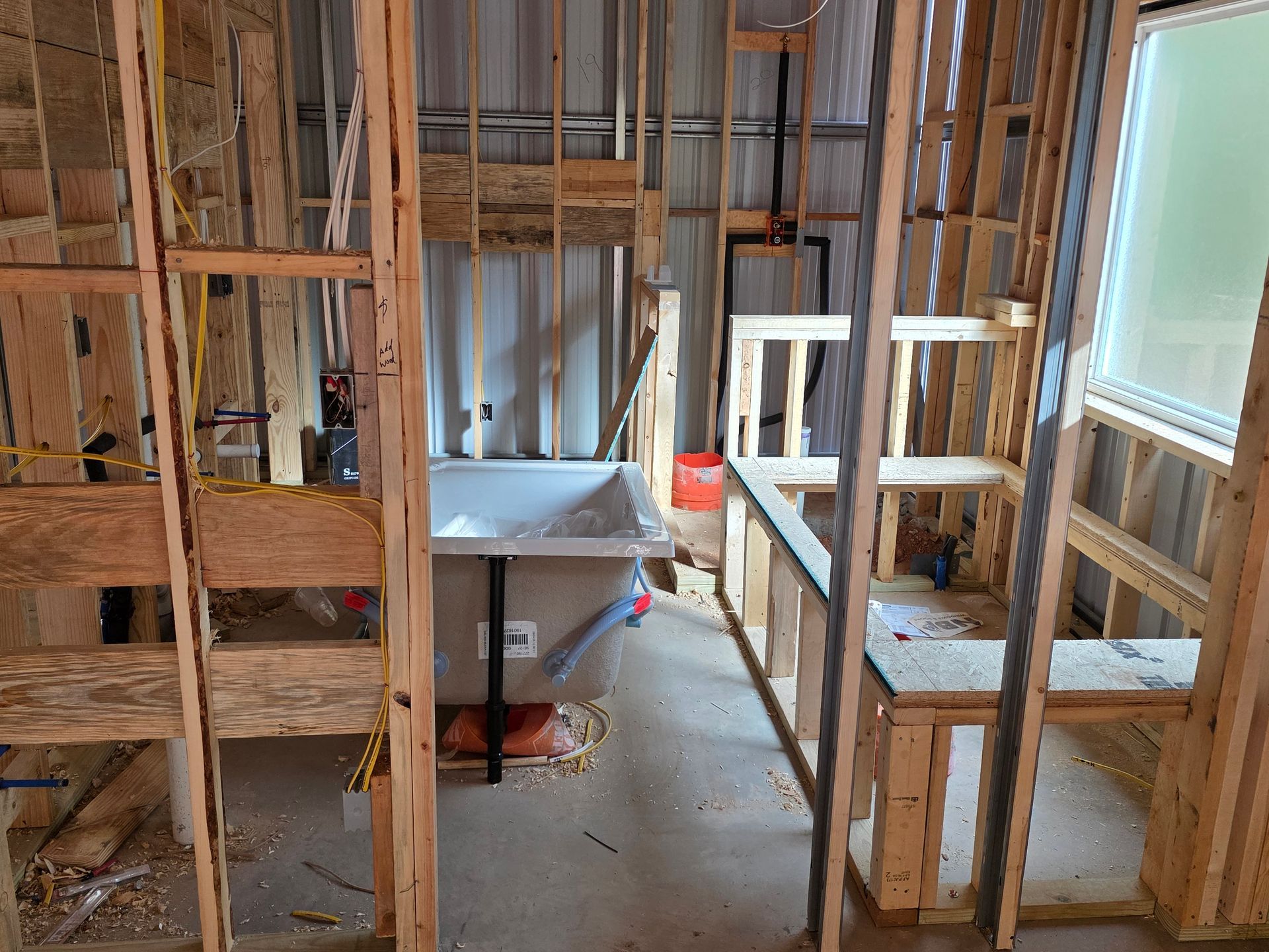 Bathroom under construction; wooden framing surrounds a bathtub and built-in bench near a window.