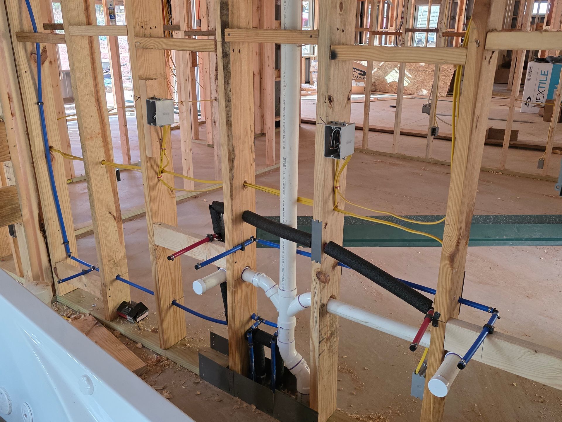 Interior view of a building under construction, showing exposed plumbing, electrical wiring, and wooden framing.