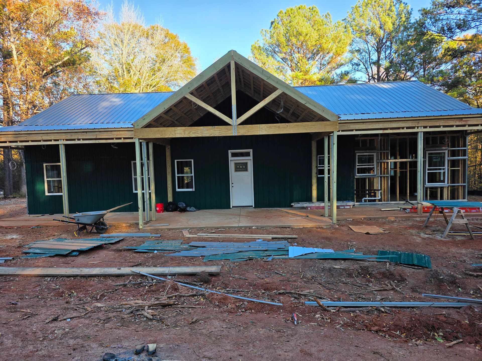 House under construction, green siding, metal roof, porch, surrounded by trees.