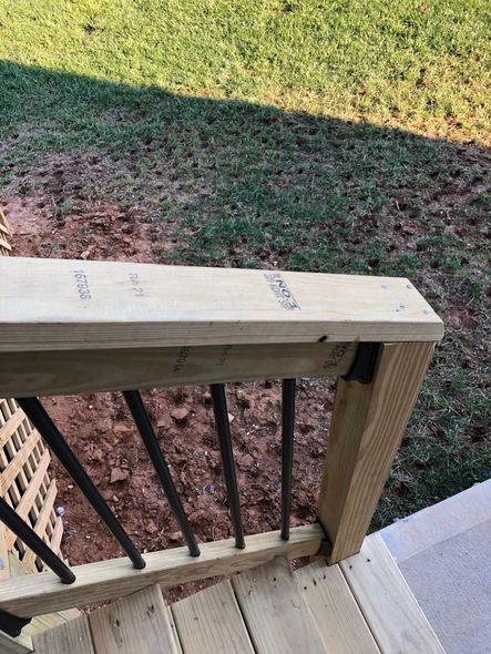 Wooden deck railing with black vertical spindles, and stairs in an outdoor setting.