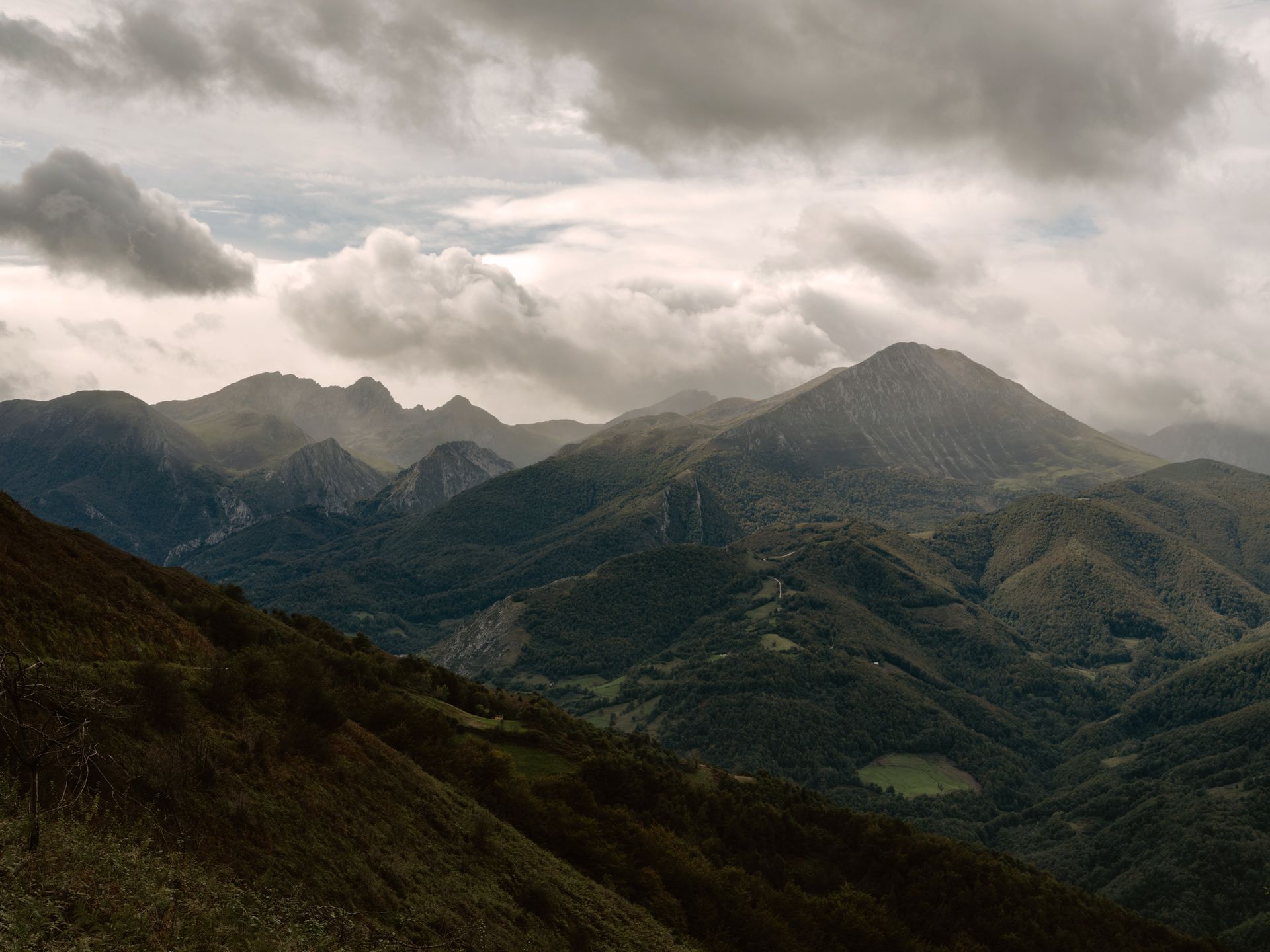 Mountains under a cloudy sky, with shades of green and brown dominating the landscape.
