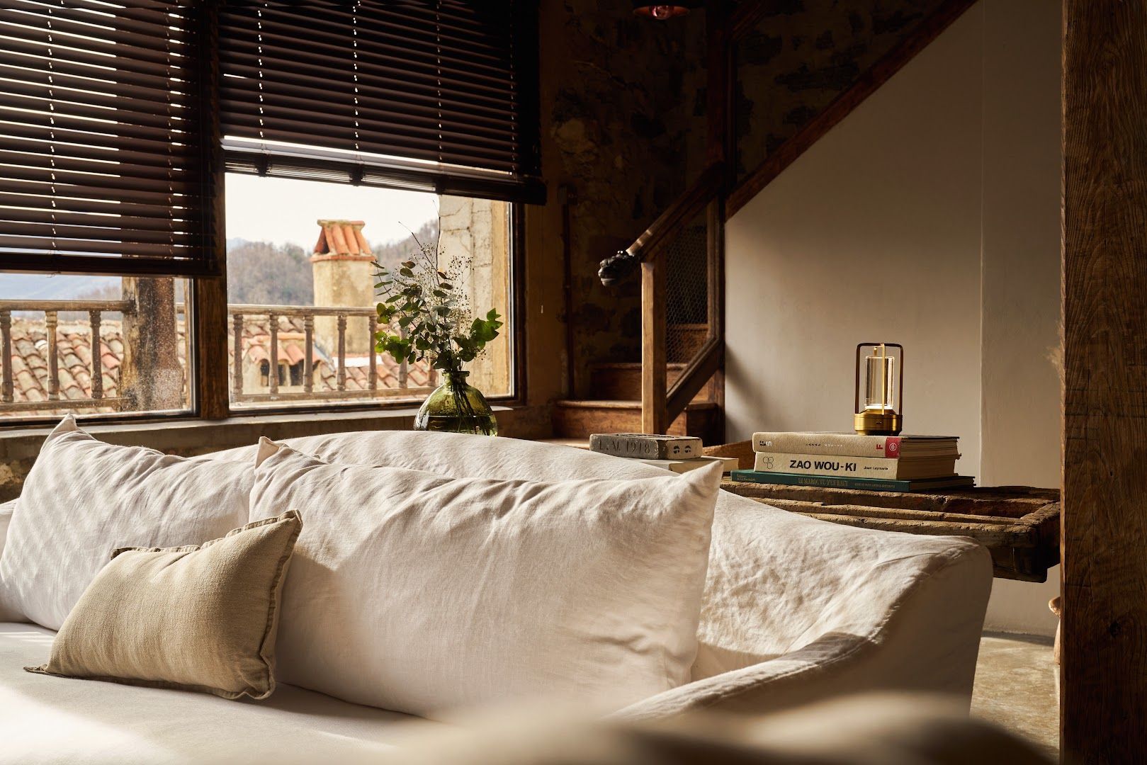 Cozy interior with white sofa near a window with view of balcony and buildings; wooden blinds.