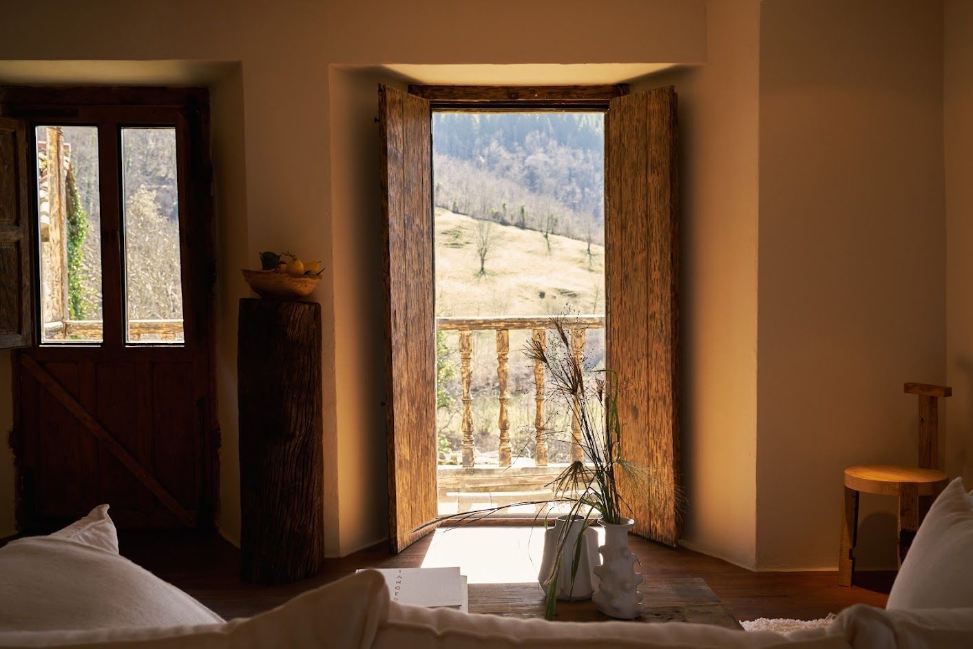 Interior with open wooden door and window looking out onto a mountain landscape.