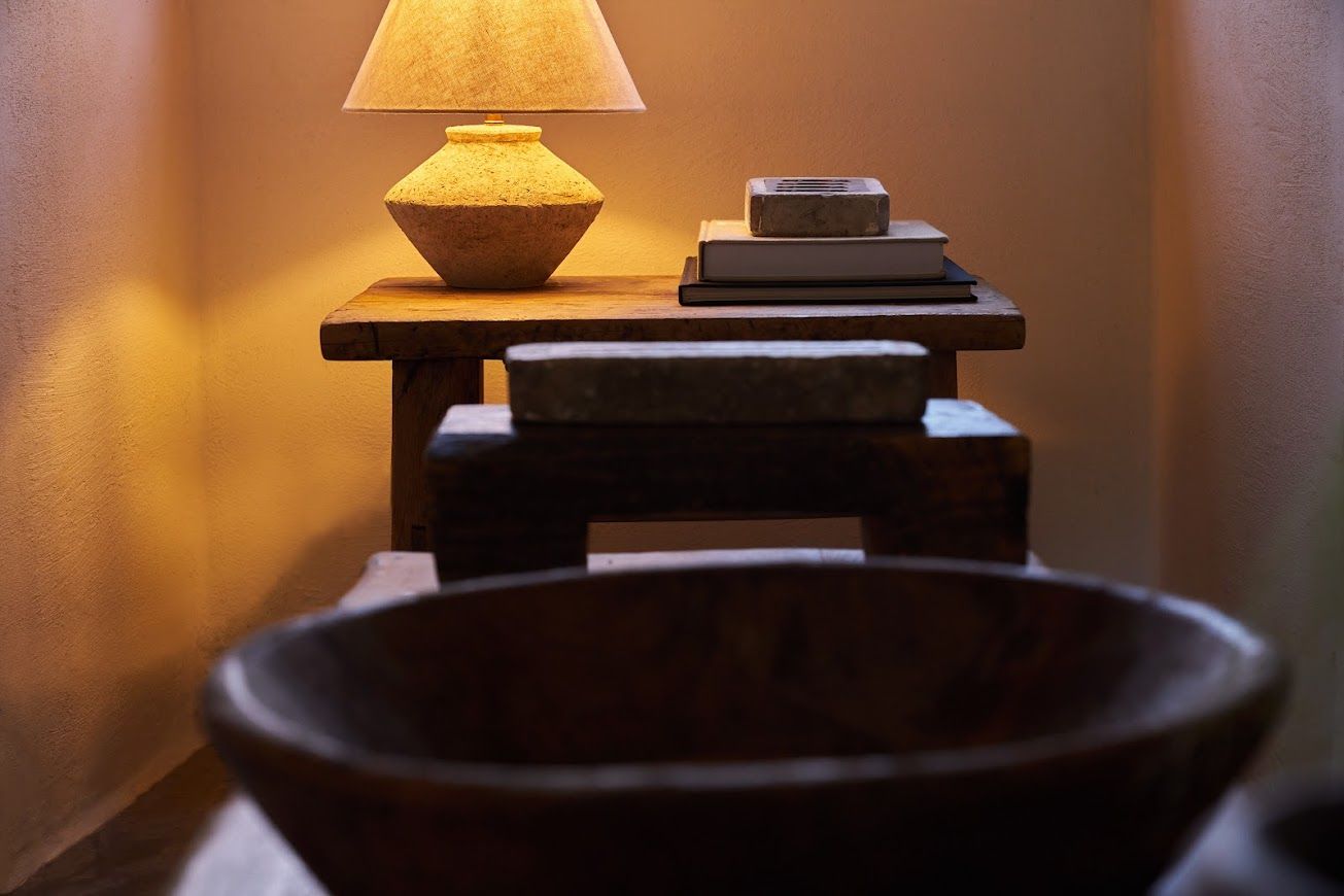 Wooden table with lamp, books, and bowl; warm lighting.