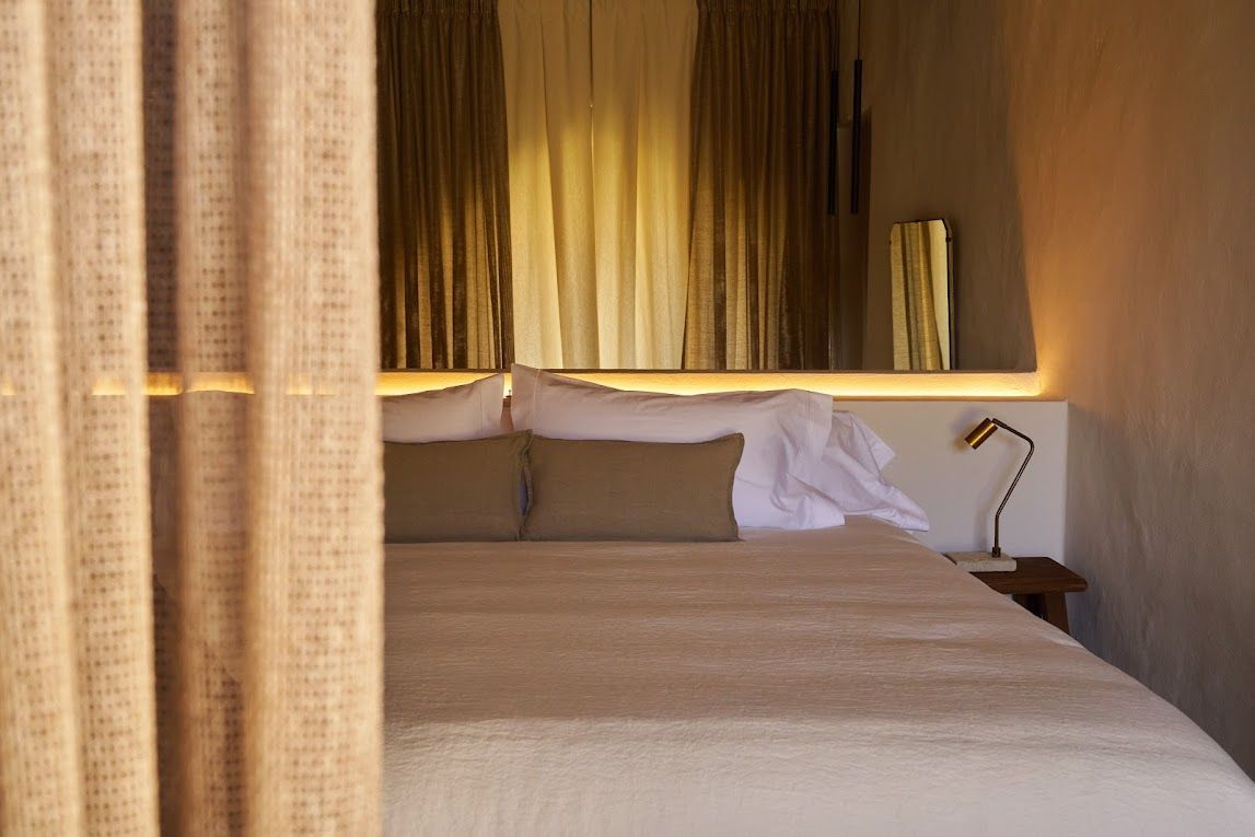 Bedroom with neutral tones. Bed with pillows, white headboard, and gold curtains.