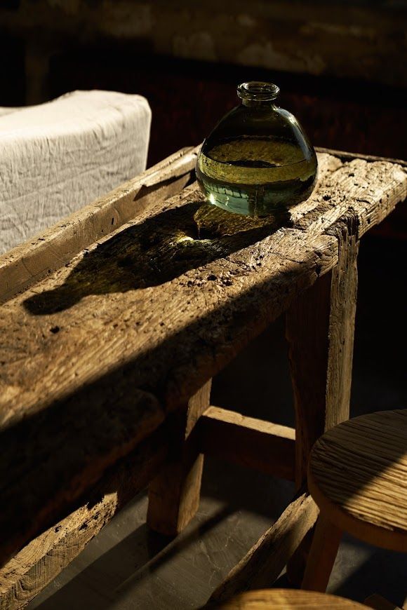 Green glass bottle on a weathered wooden table; sunlight casts a dark shadow.
