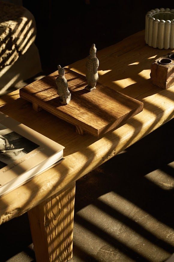 Wooden table with figurines and a book, lit by window shadows.