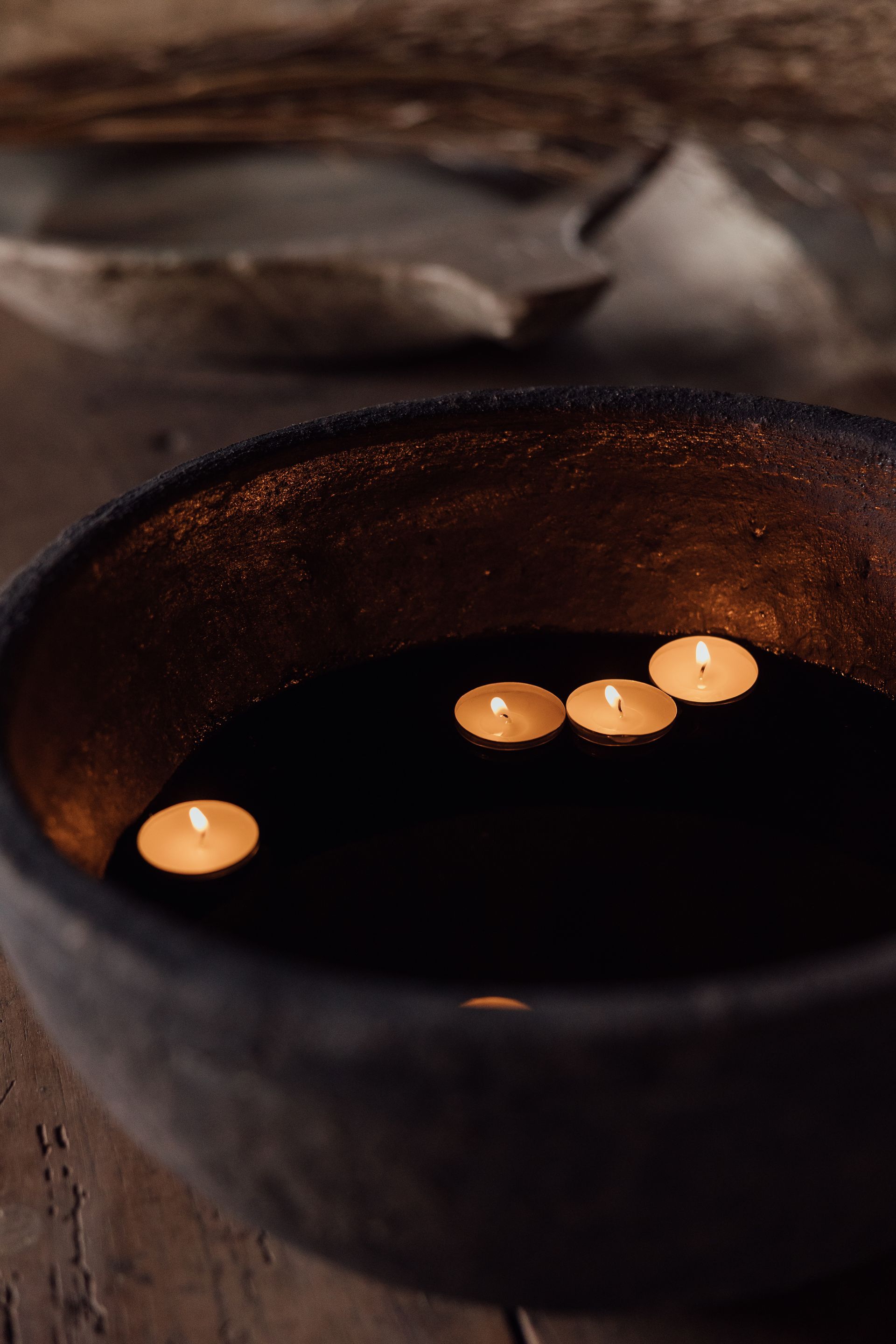 Black bowl with floating lit candles, wooden surface.