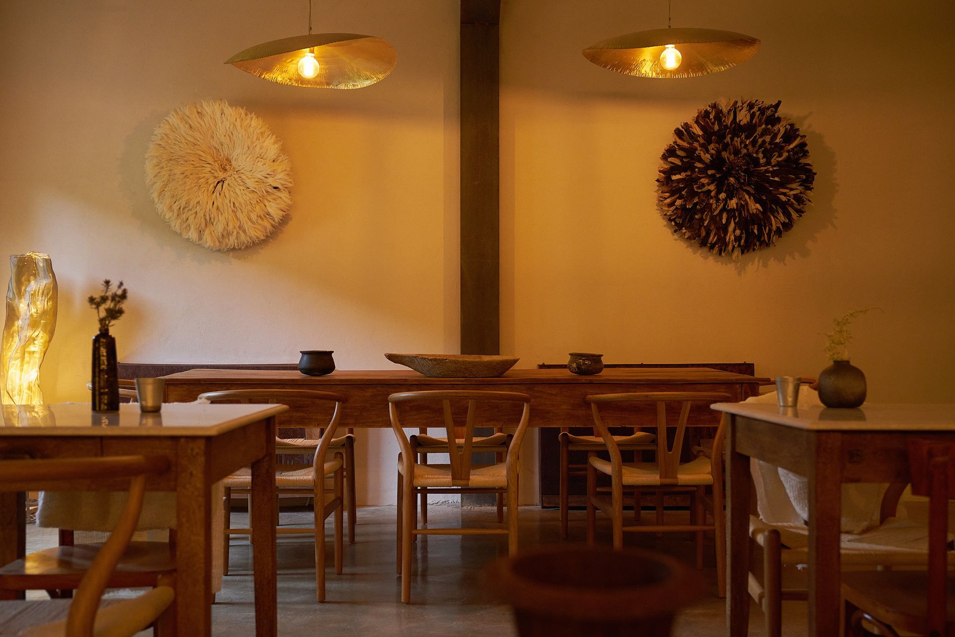 Cozy restaurant interior with wooden tables, chairs, and decorative wall hangings under warm lighting.
