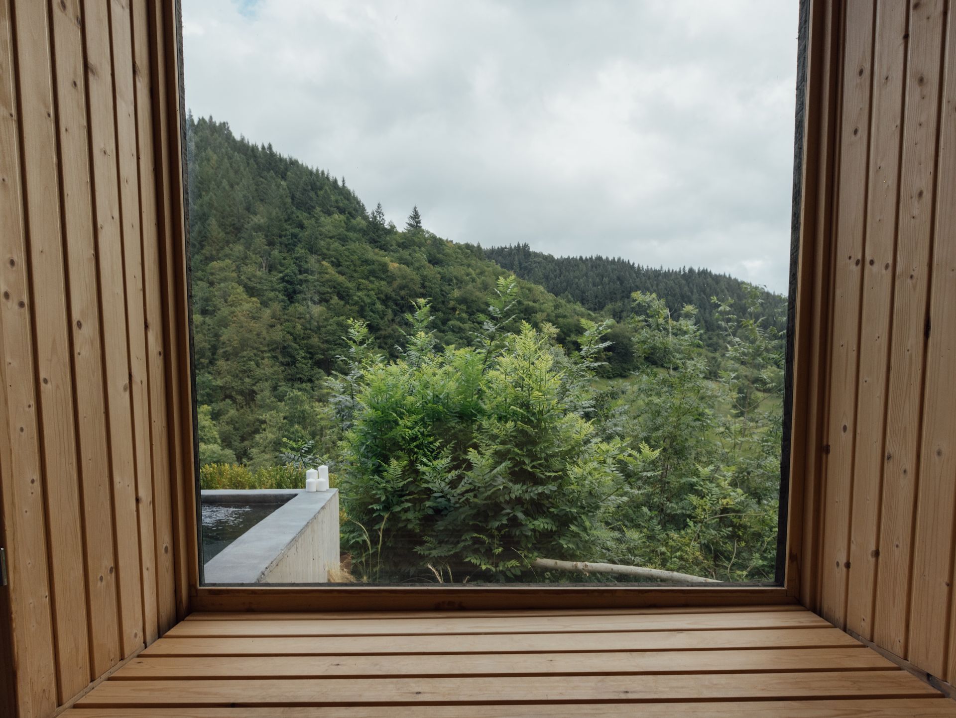 Wooden window frame overlooking a green mountain forest on an overcast day.