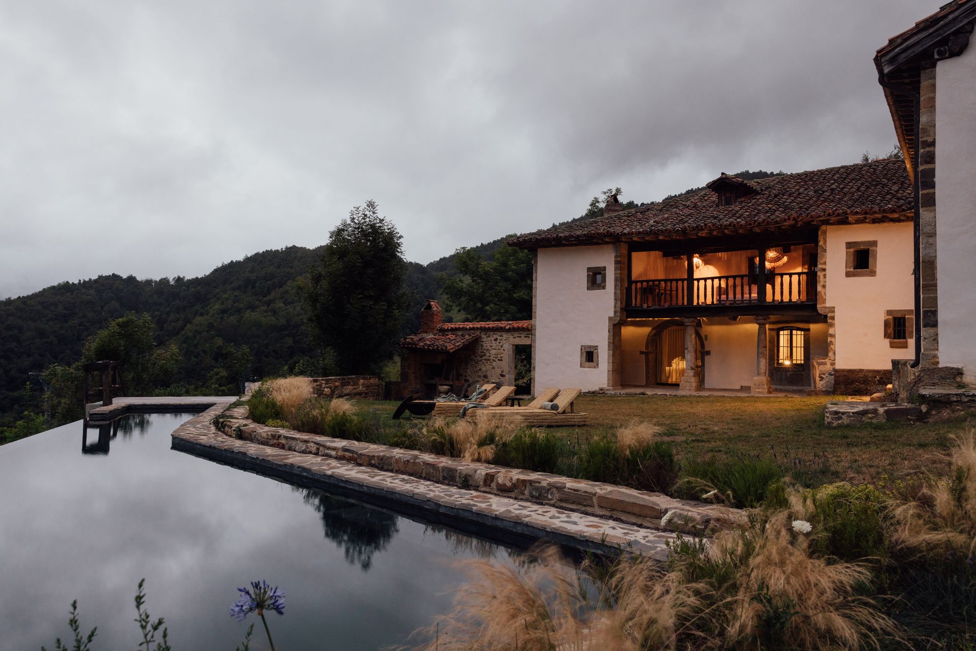 House with infinity pool overlooking mountains under cloudy sky.